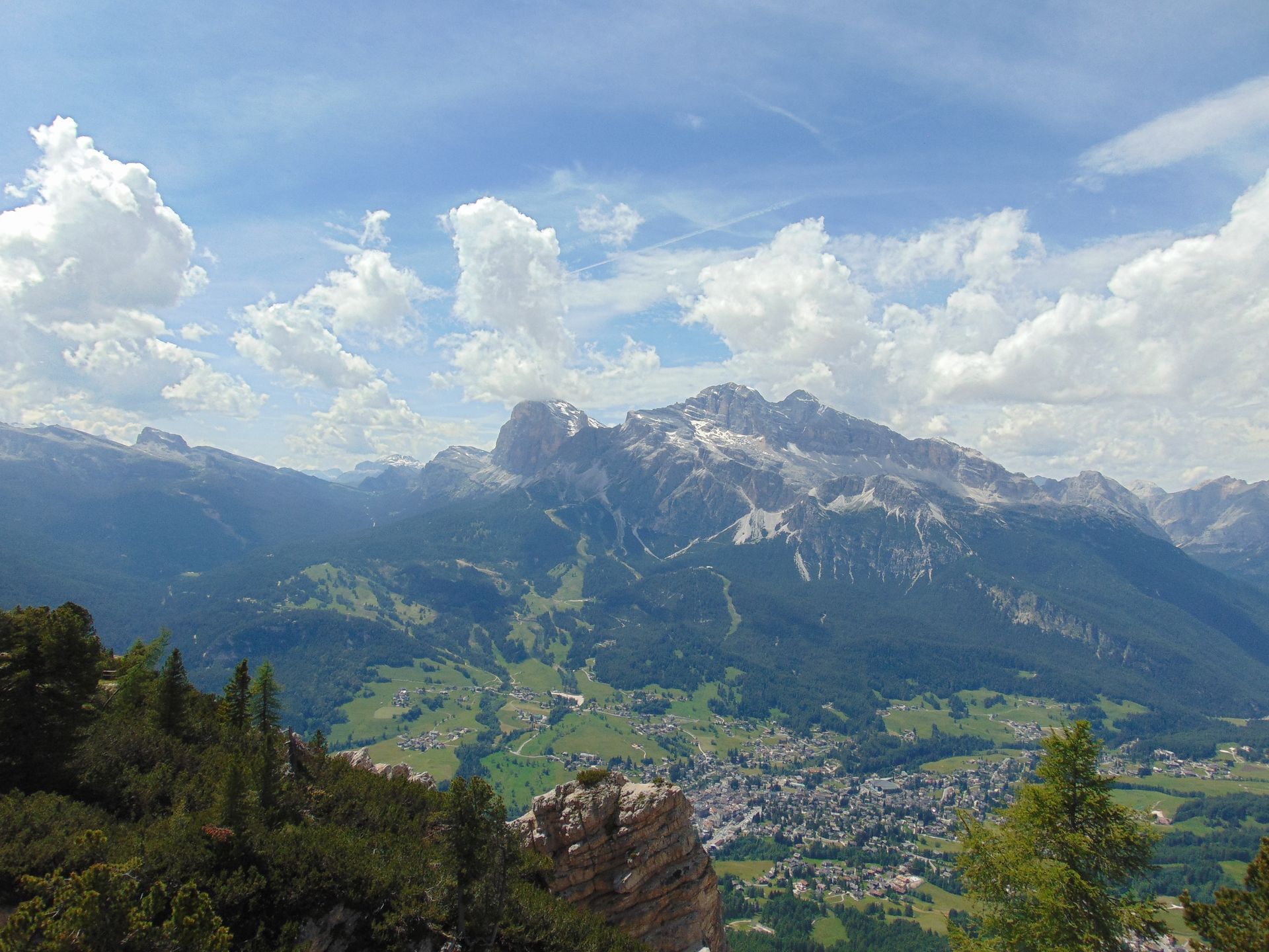 Mountain range under a partly cloudy sky, overlooking a valley with a town.