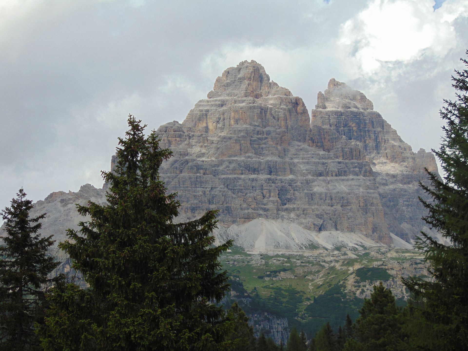 Rocky mountain peak with green trees under a cloudy sky.