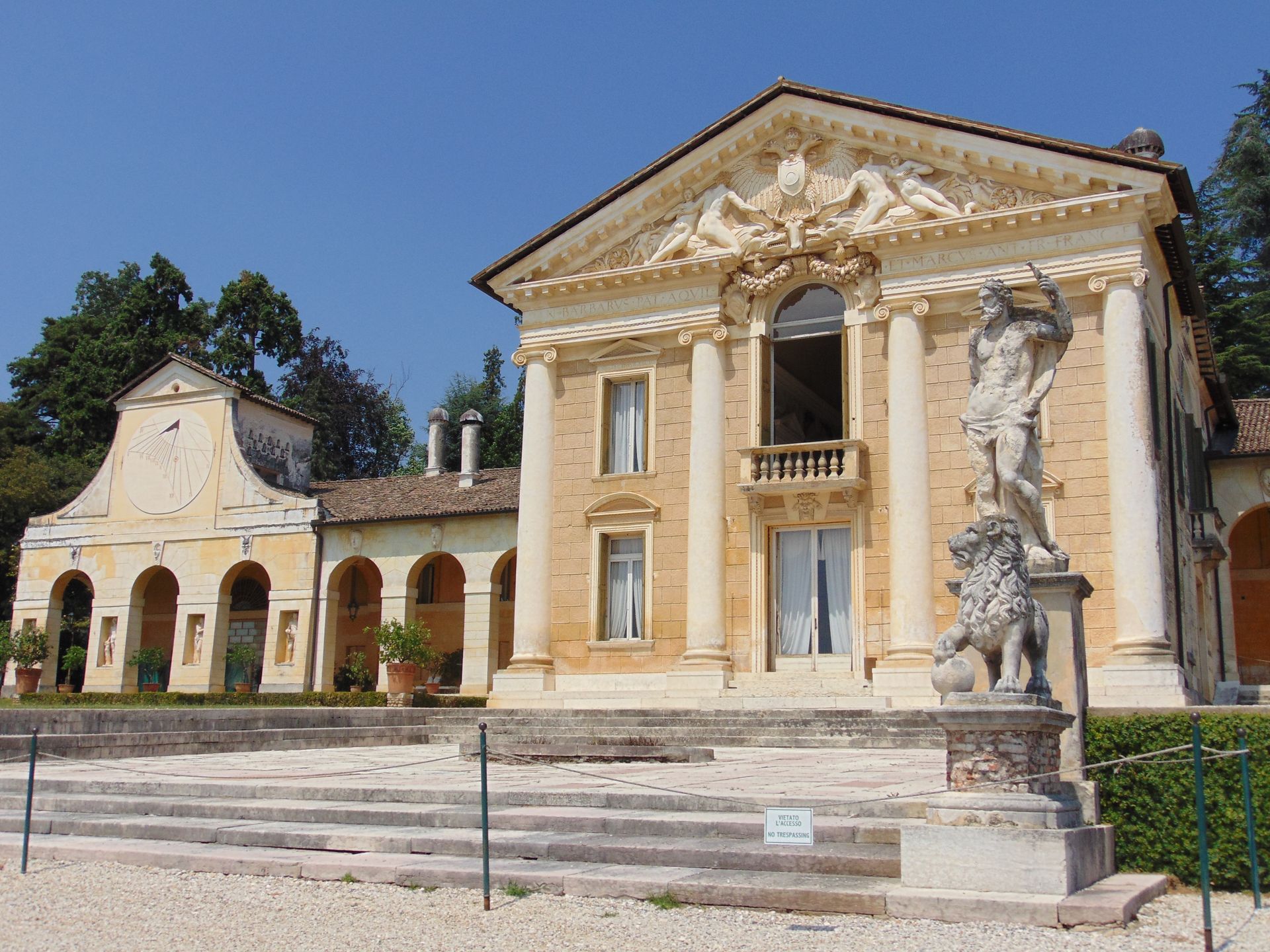 Neoclassical villa with columns, sculpture, and arched structure under blue sky.