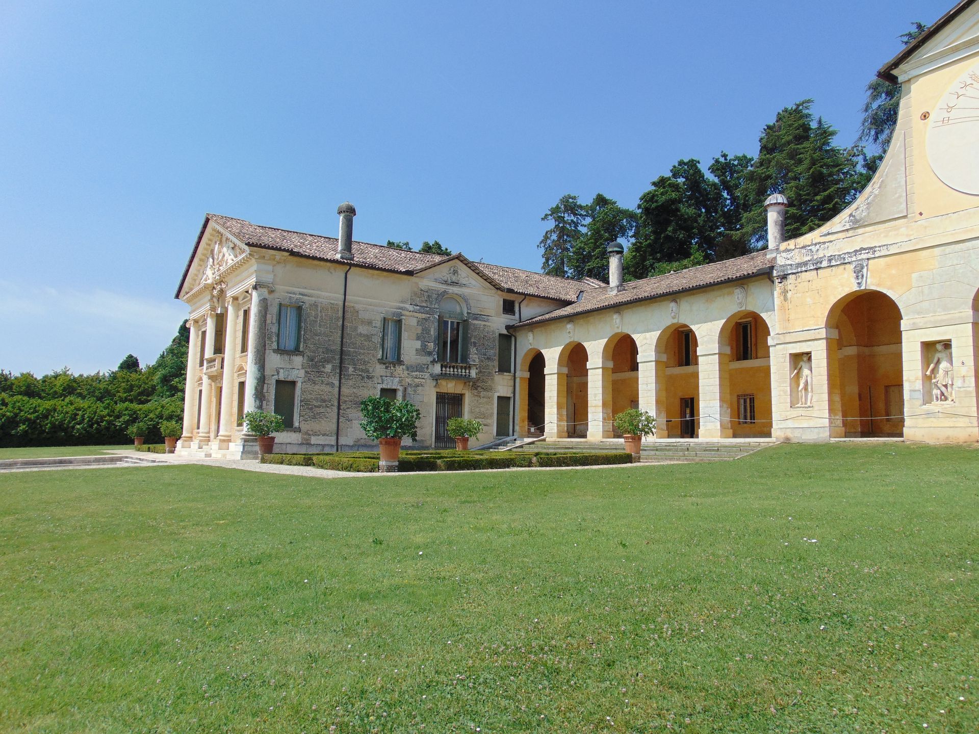 Elegant, aged villa with a colonnade and grassy lawn under a clear blue sky.