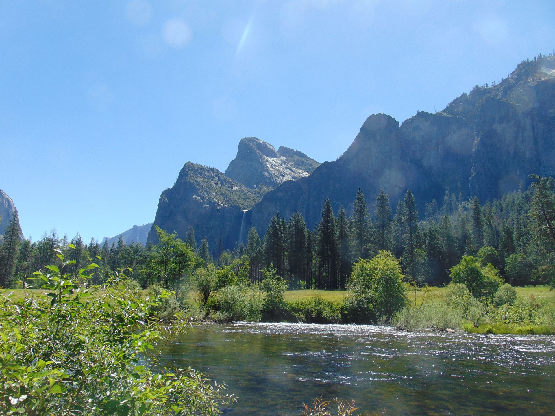 River in a valley with mountains and trees under a clear, blue sky.