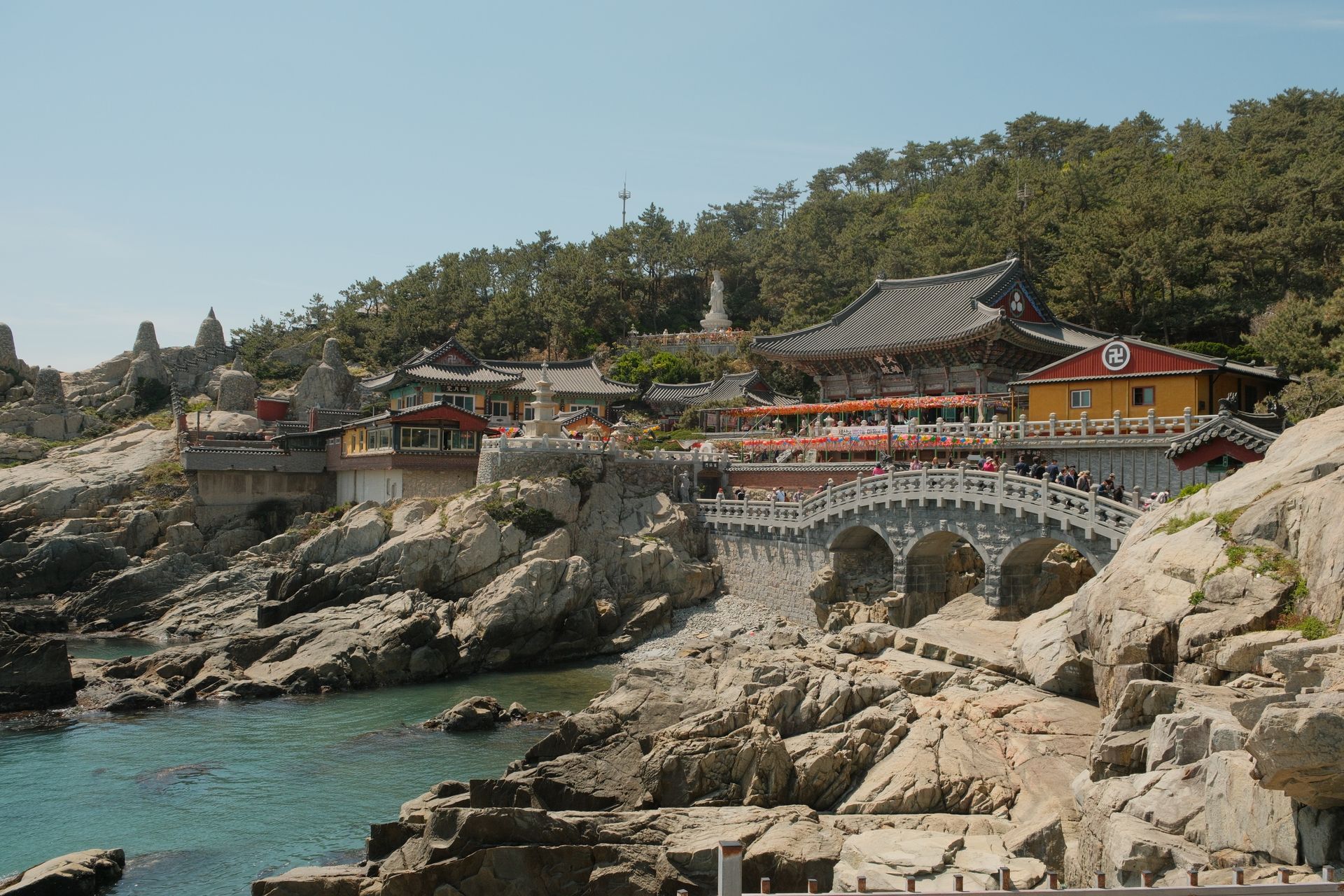 Temple complex on rocky coast, white arched bridge, blue water in Busan, South Korea.