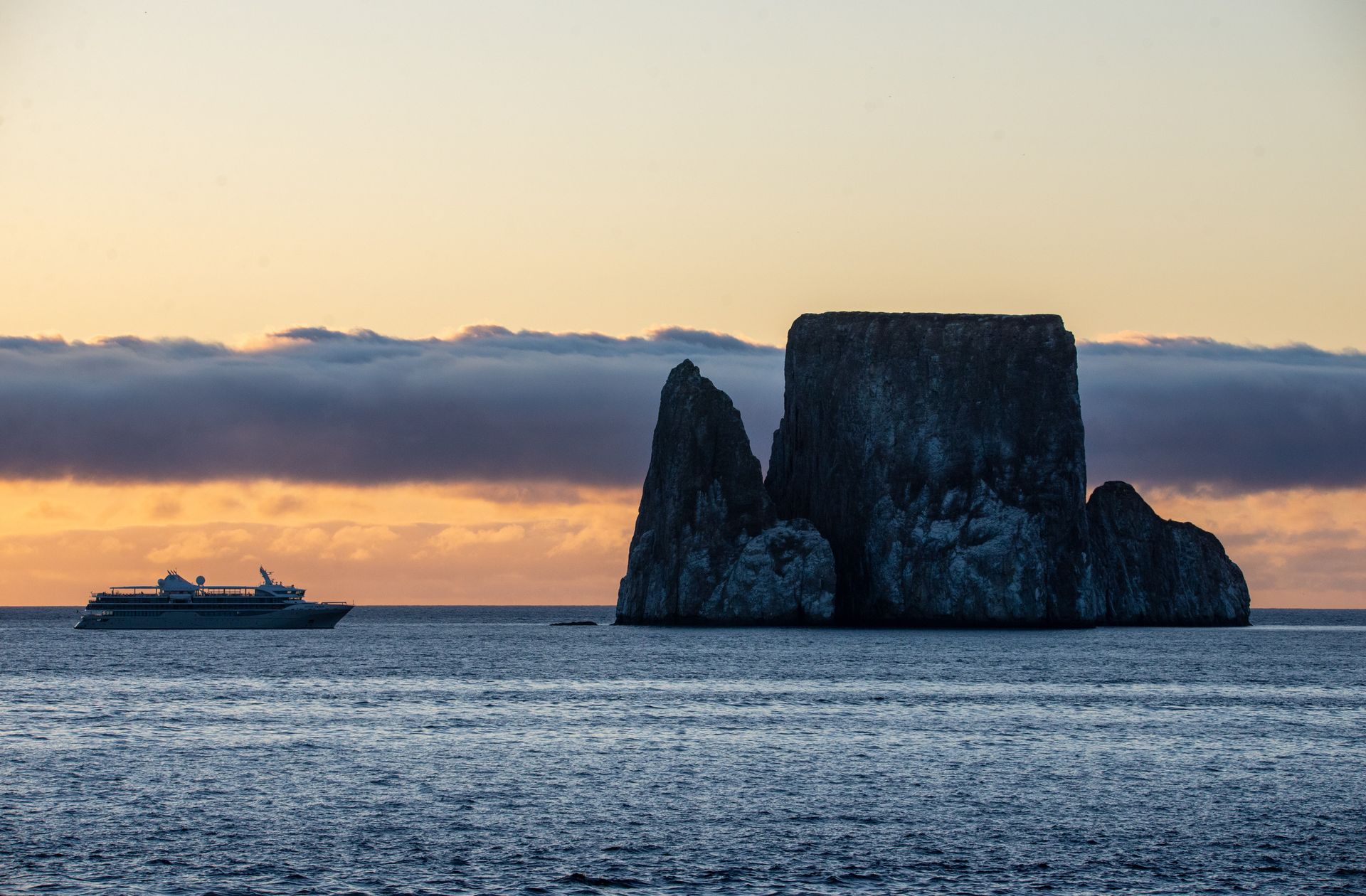 Ocean view with a boat and a large rock formation; dusky orange sky.