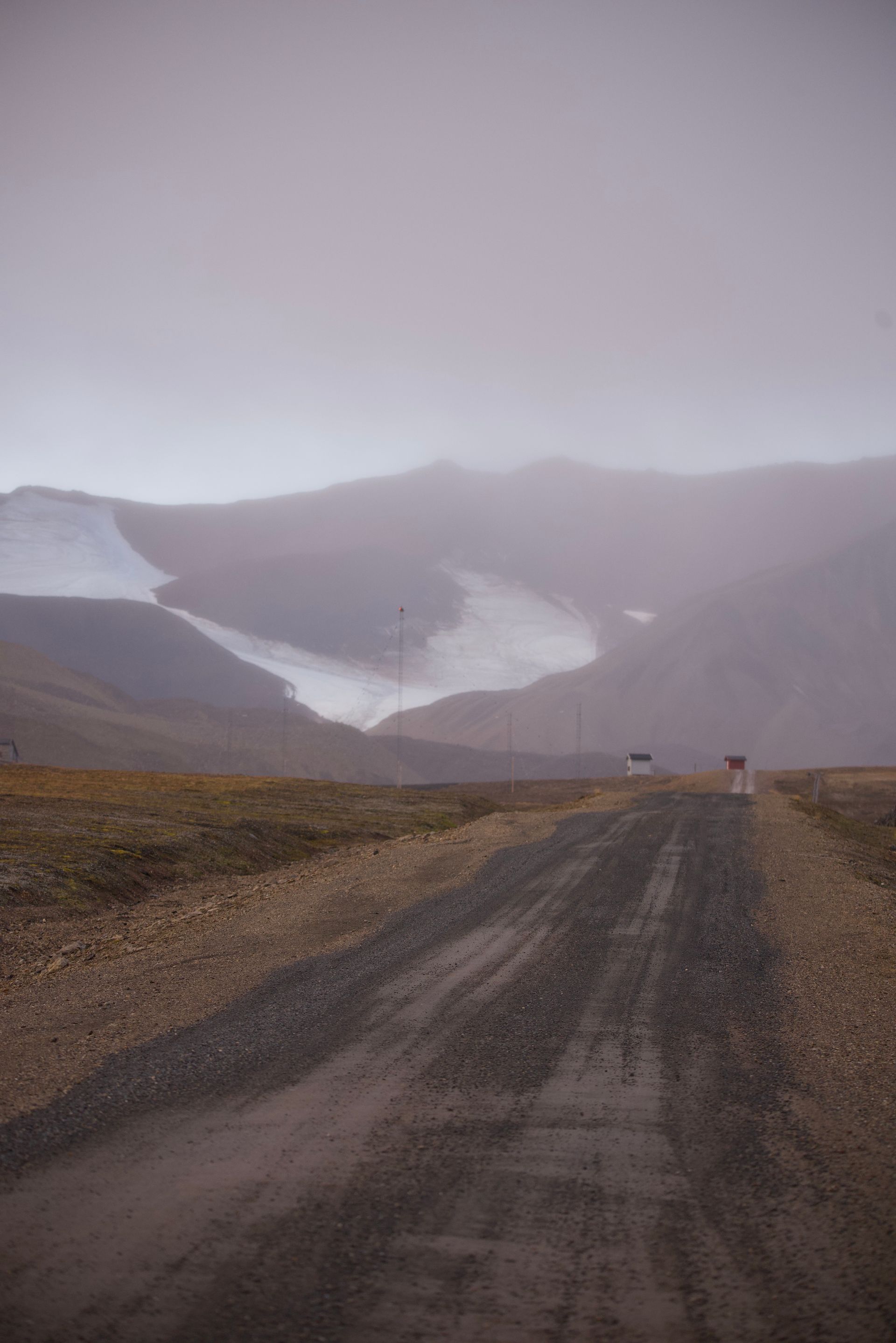 Gravel road leading toward mountains obscured by fog, with a patch of snow visible.