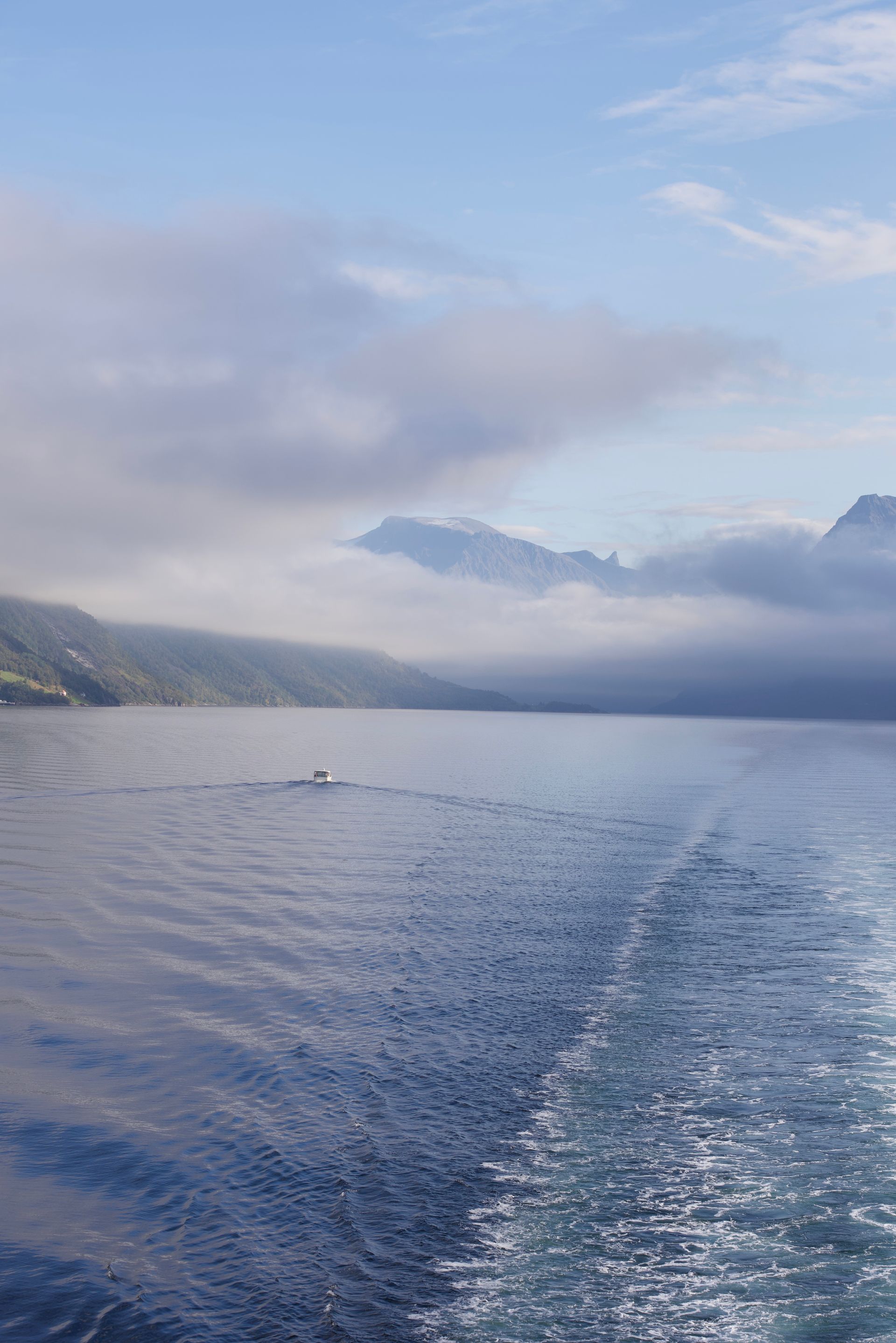 Watery wake of a boat on a lake under cloudy skies, with mountains in the background.