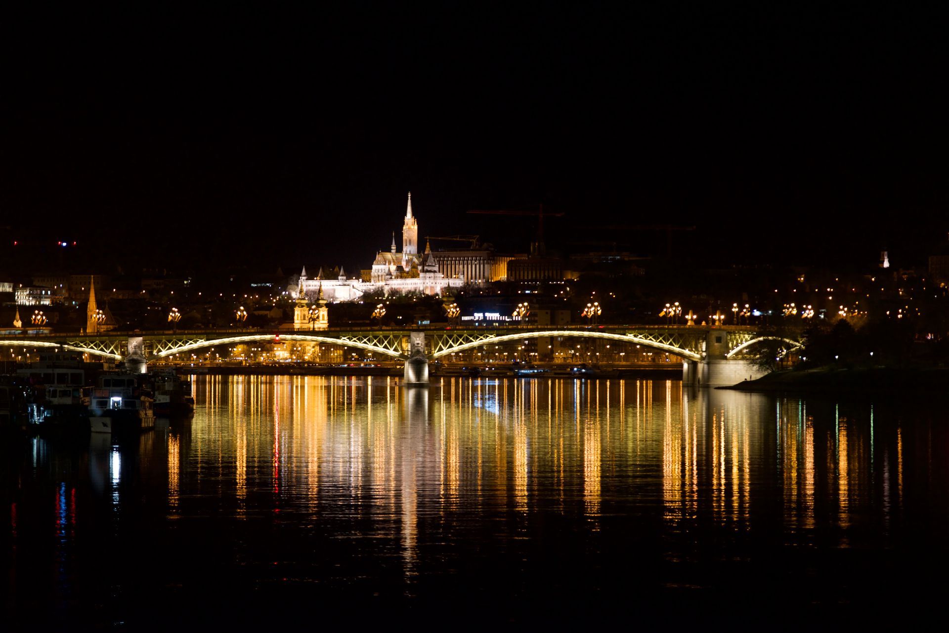 Night view of Budapest with illuminated bridge and city lights reflecting in the water.