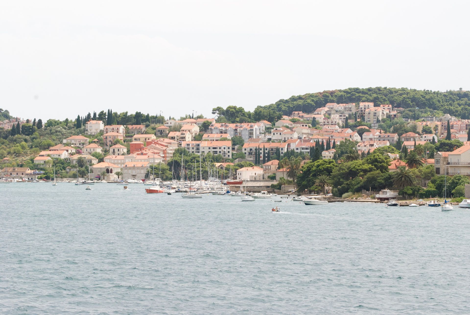 Coastal town with red-tiled roofs and white buildings on a hillside, with boats on the water.