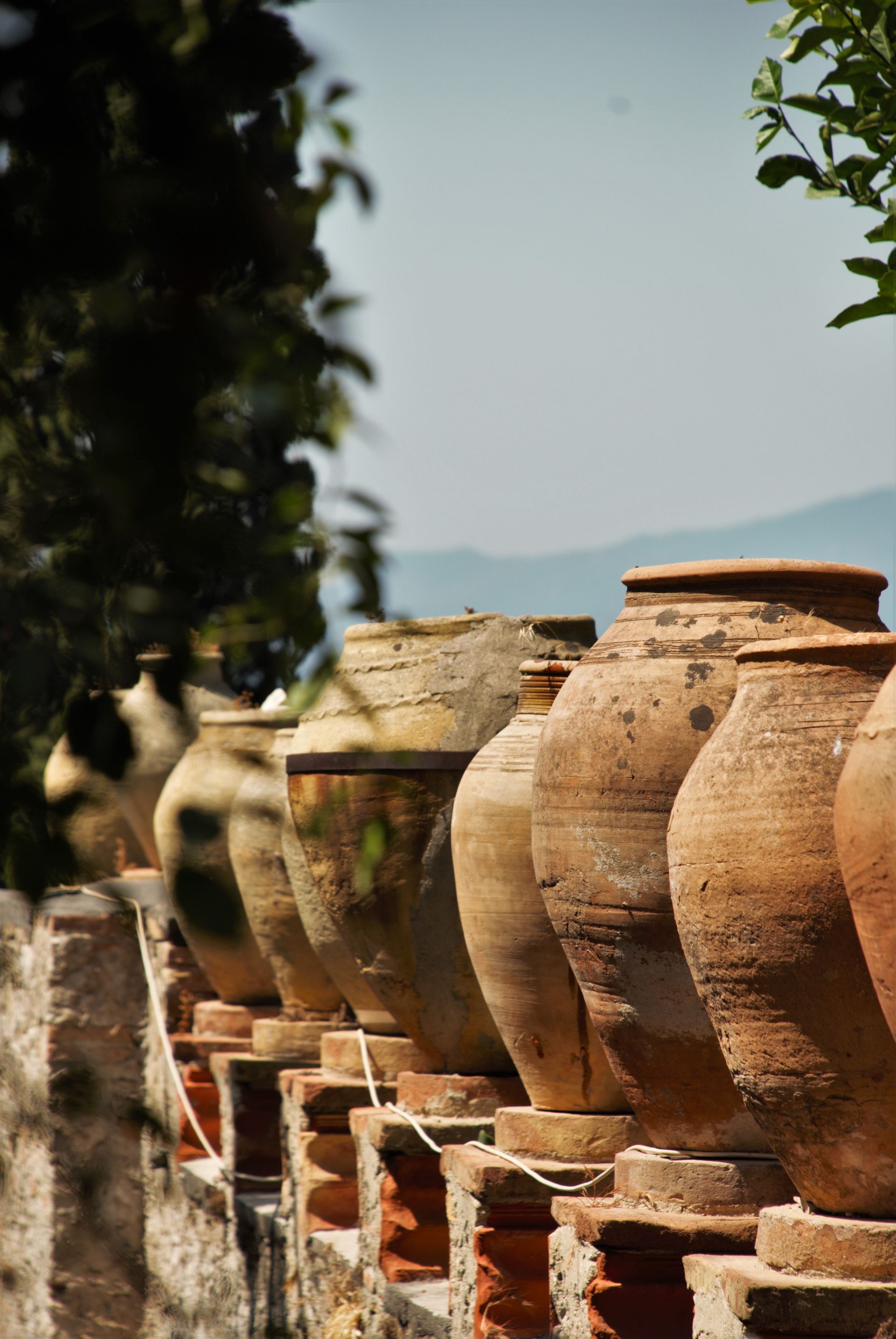 Row of weathered terracotta pots atop a stone wall, against a blurred landscape.