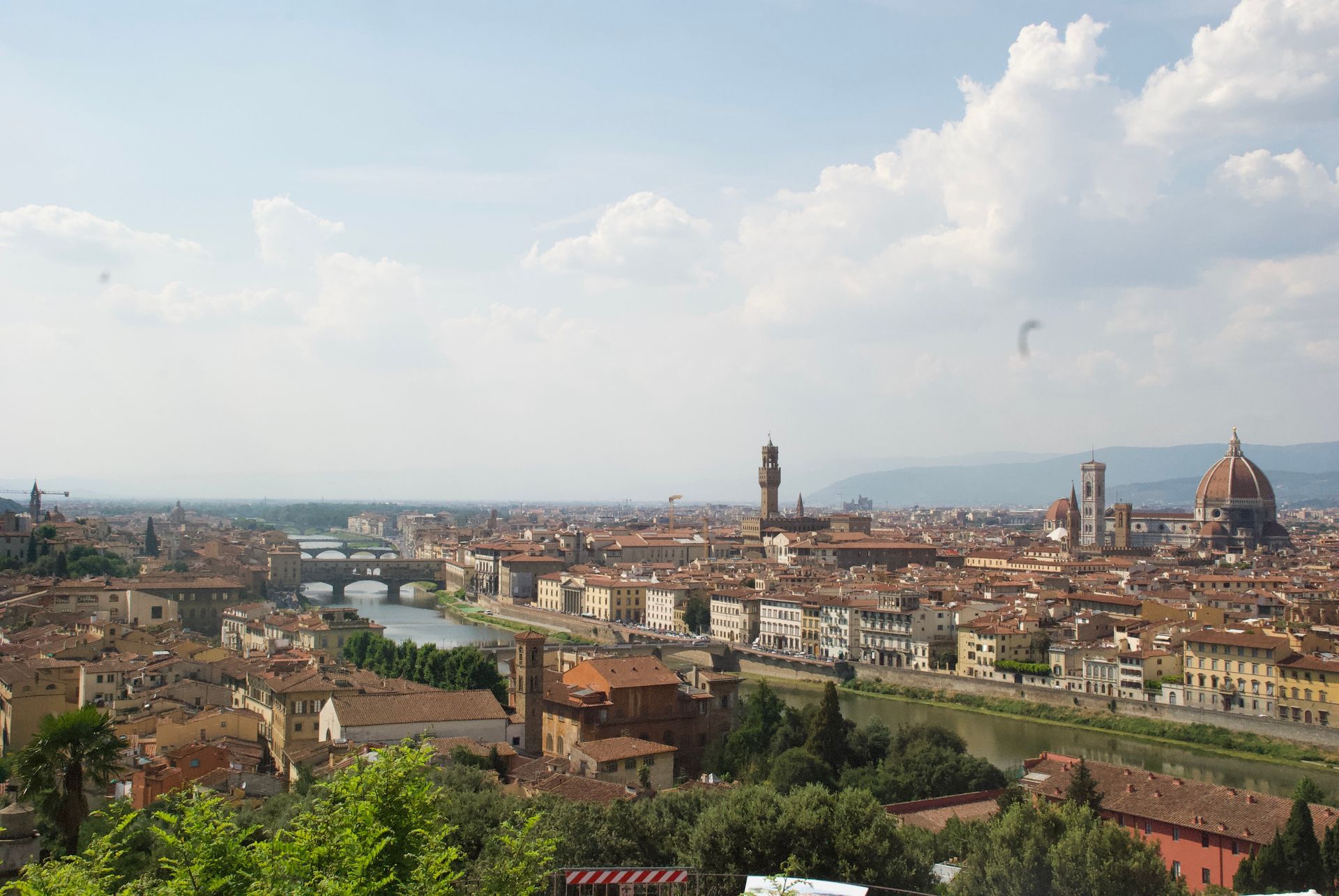 Panoramic view of Florence, Italy, with the Arno River, bridges, and the Duomo under a partly cloudy sky.