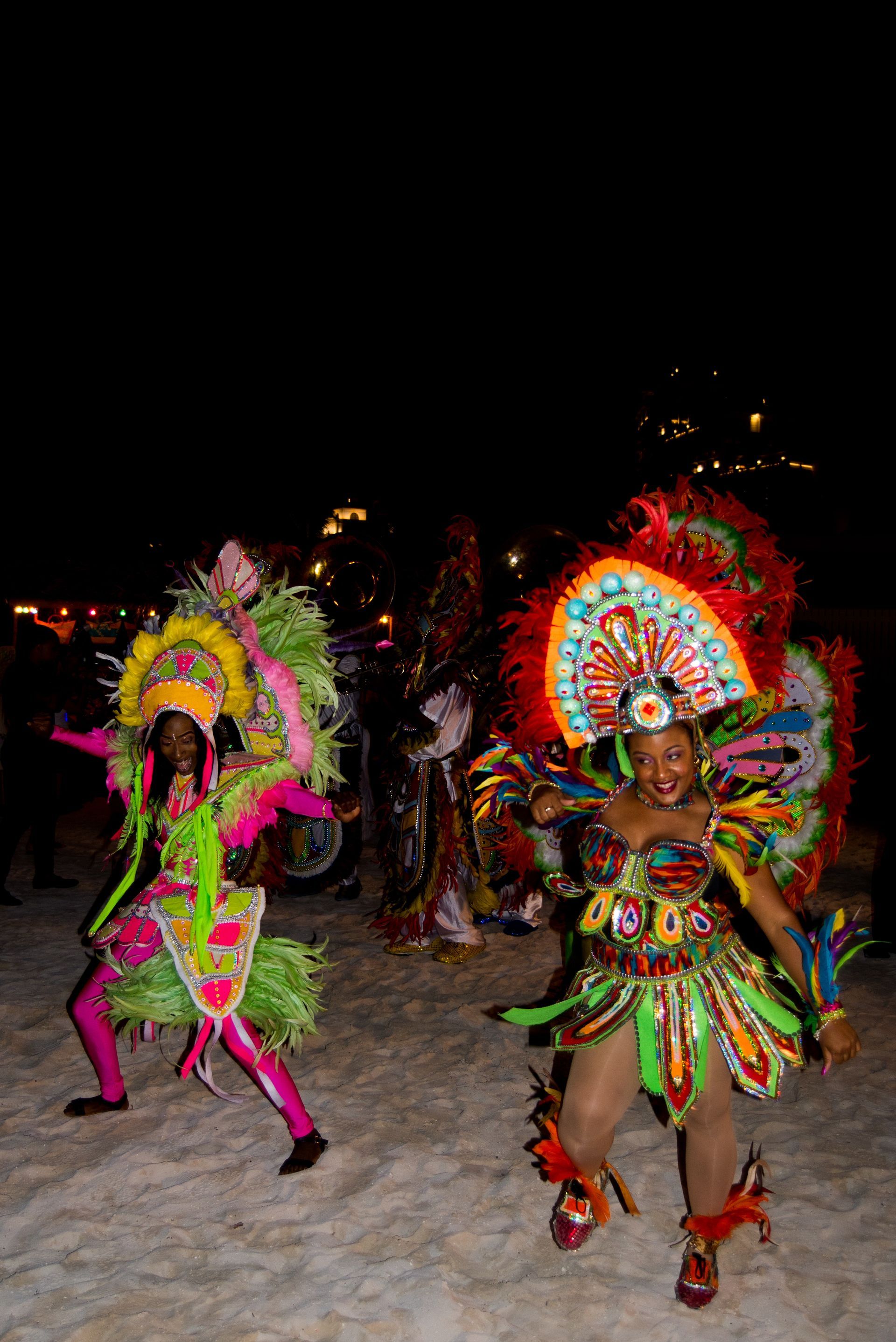 Two people in colorful carnival costumes dance at night.