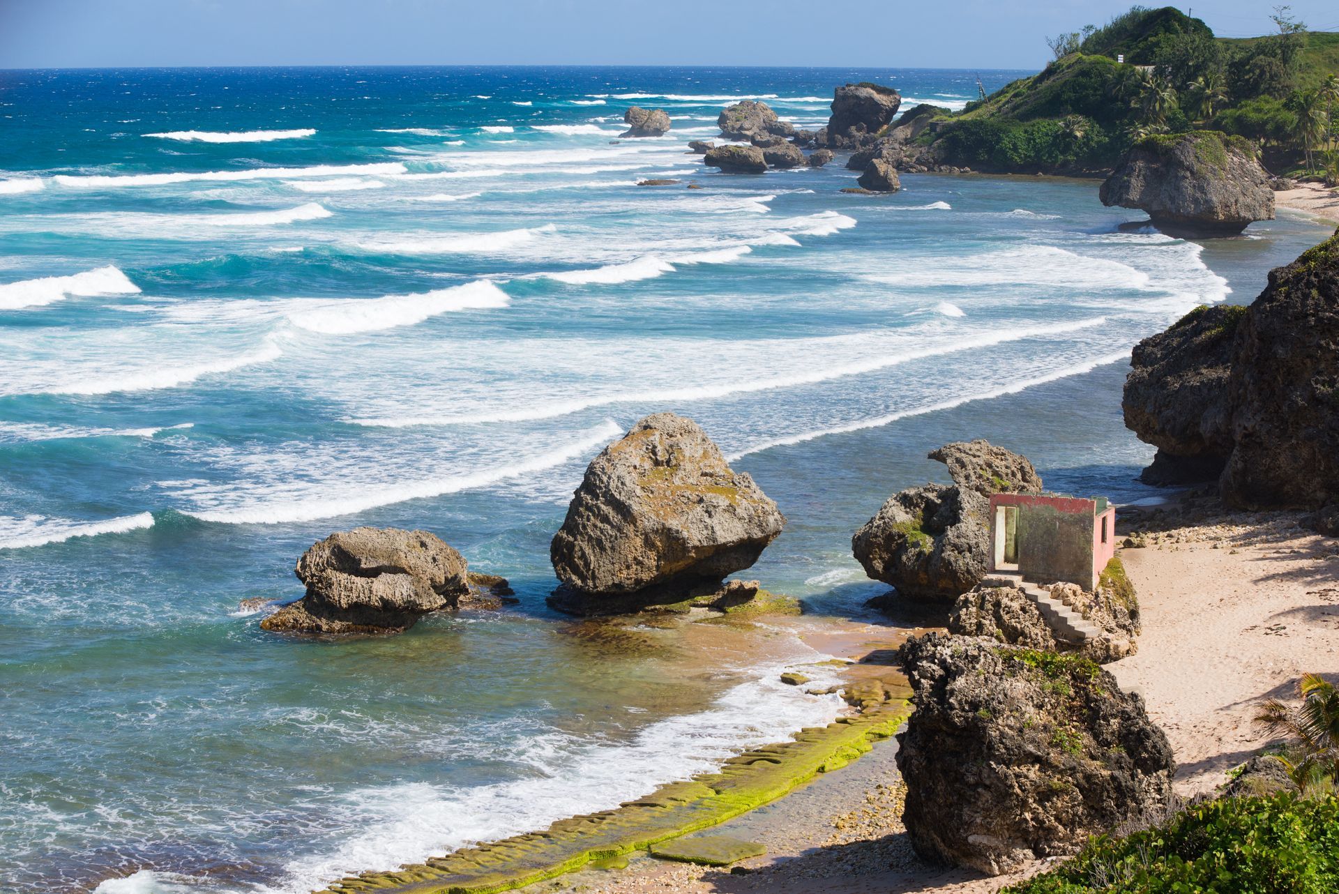 Rocky Caribbean coastline with turquoise water, white waves, and a small building.