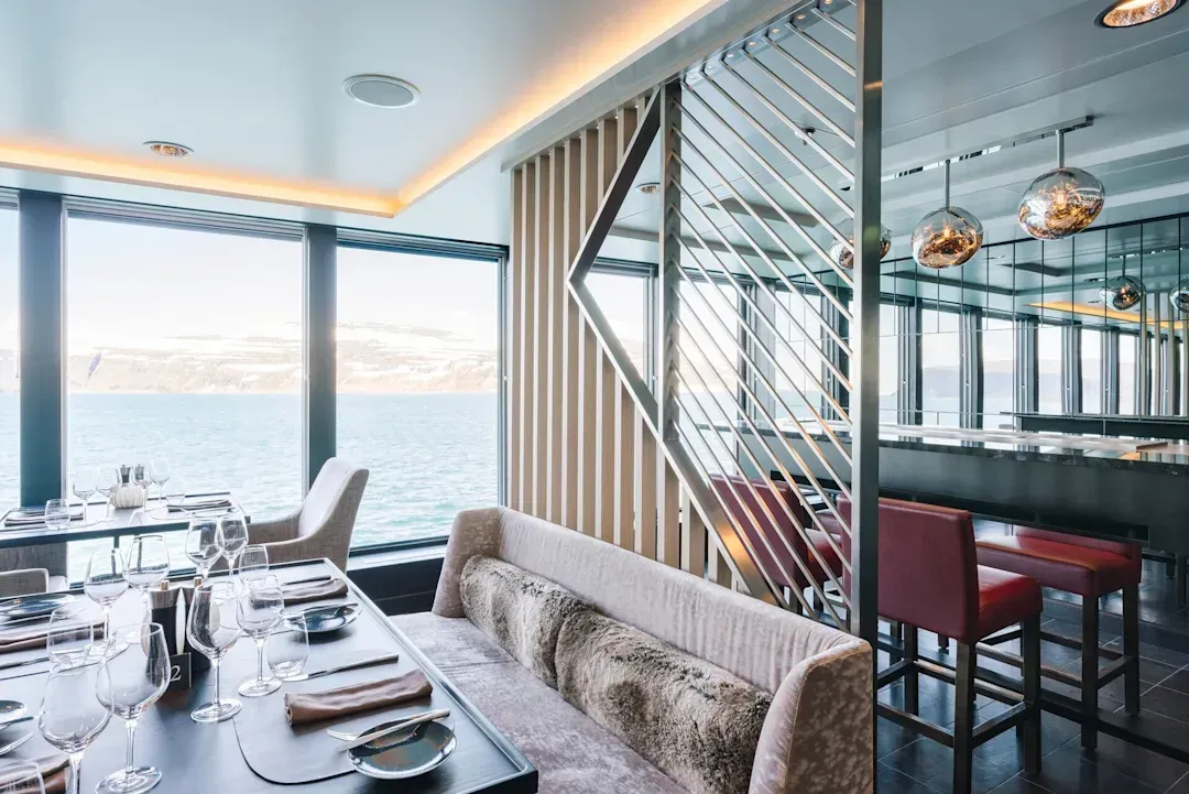 A dining room with a couch and a table with a view of the ocean on Hurtigruten Expeditions' MS Fridtjof Nansen cruise ship.