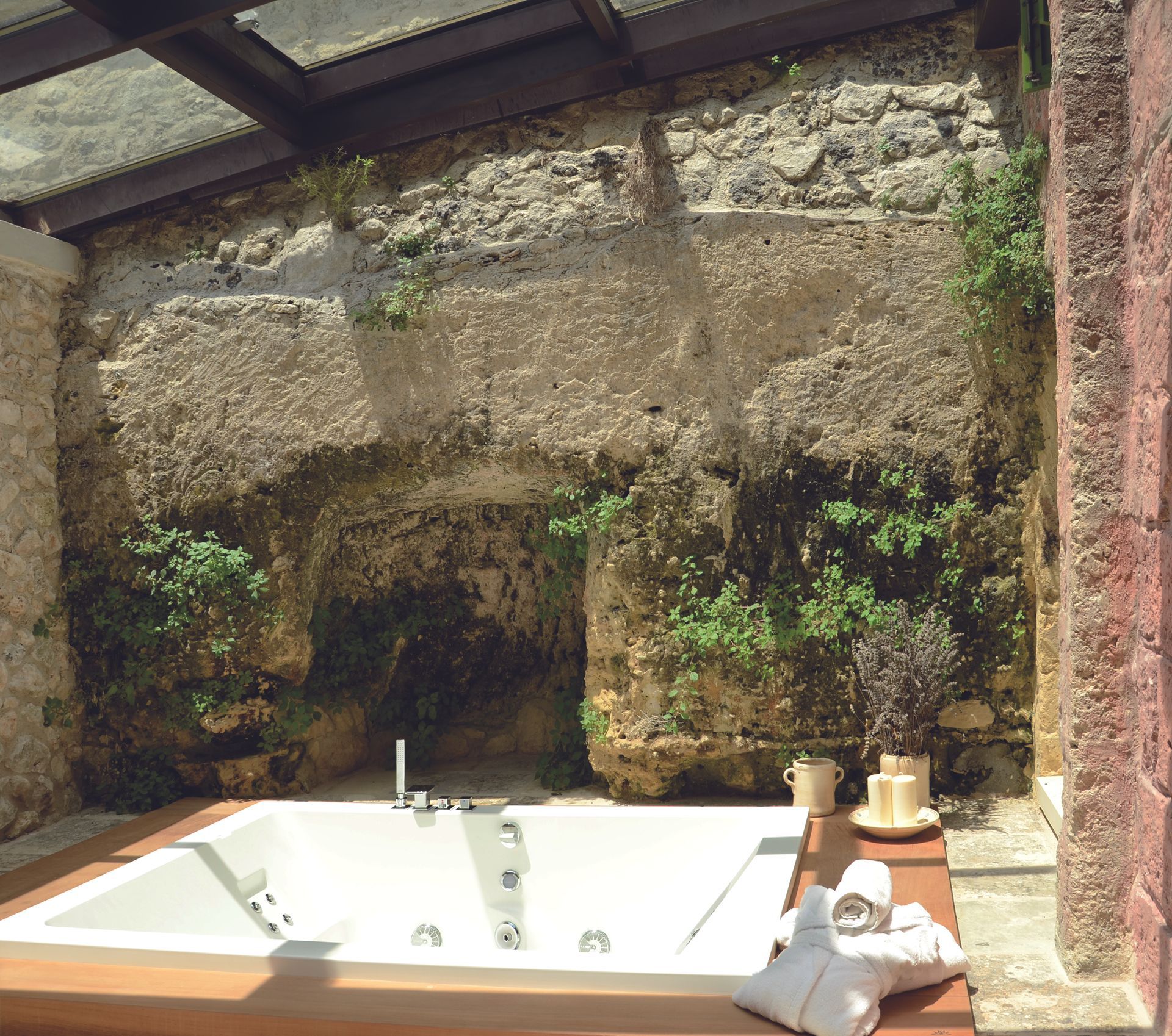 A bathtub in a bathroom with a stone wall behind it at Naturalis Bio Resort & Spa in Puglia, Italy.