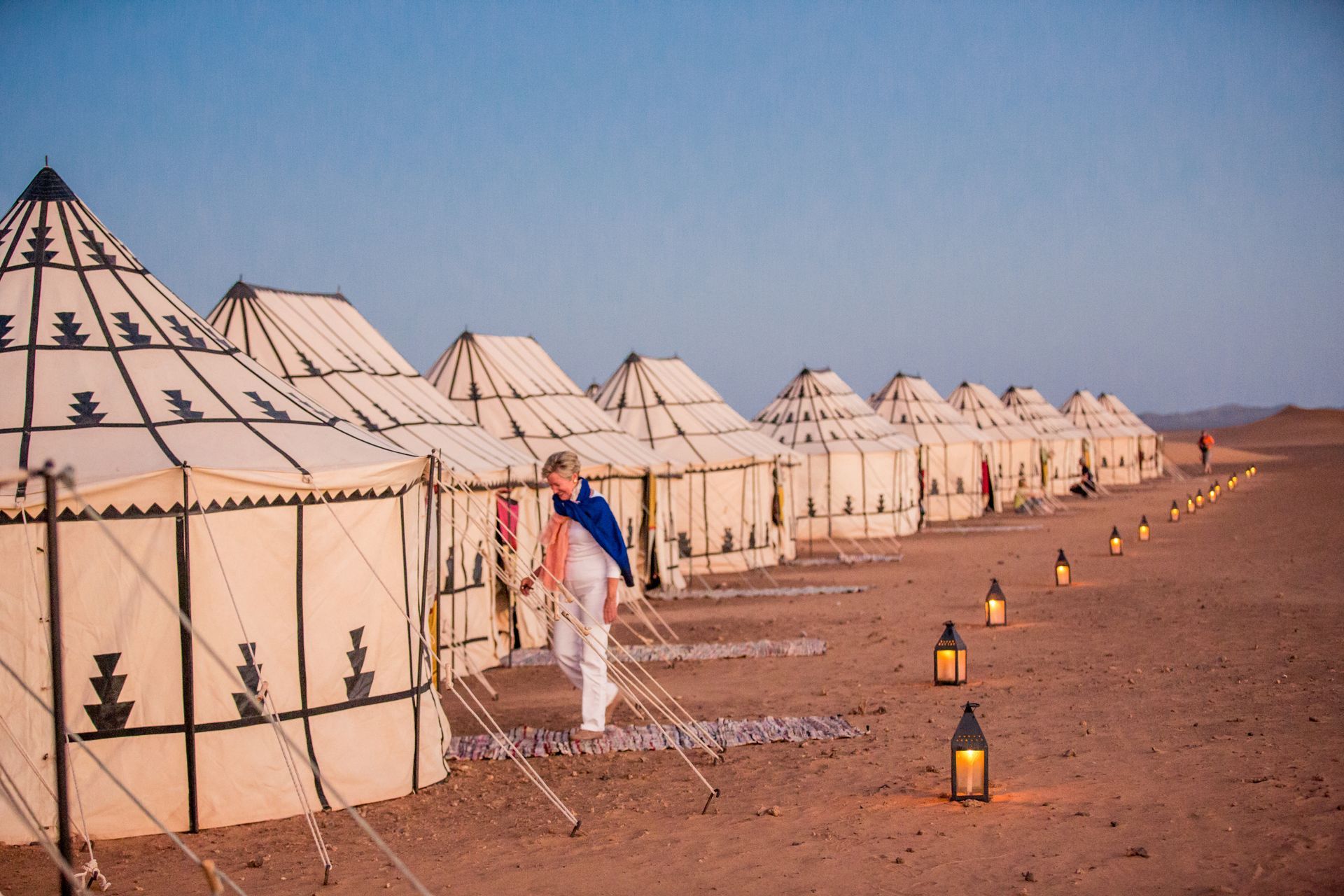 A man is standing in front of a row of tents in the desert in Morocco. 