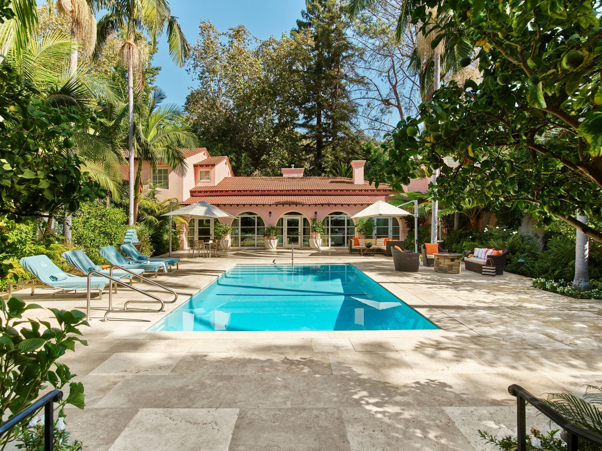 A large swimming pool surrounded by chairs in front of a house at the Dorchester Collection Hotel in Los Angeles. 