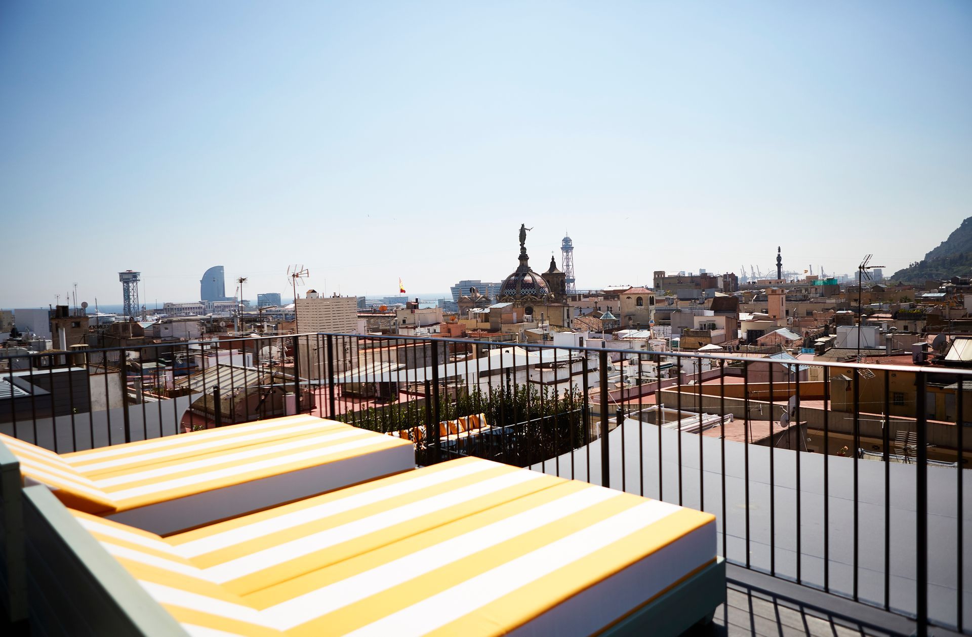 A view of a city from a balcony with striped chairs at Wittmore Hotel in Barcelona, Spain.