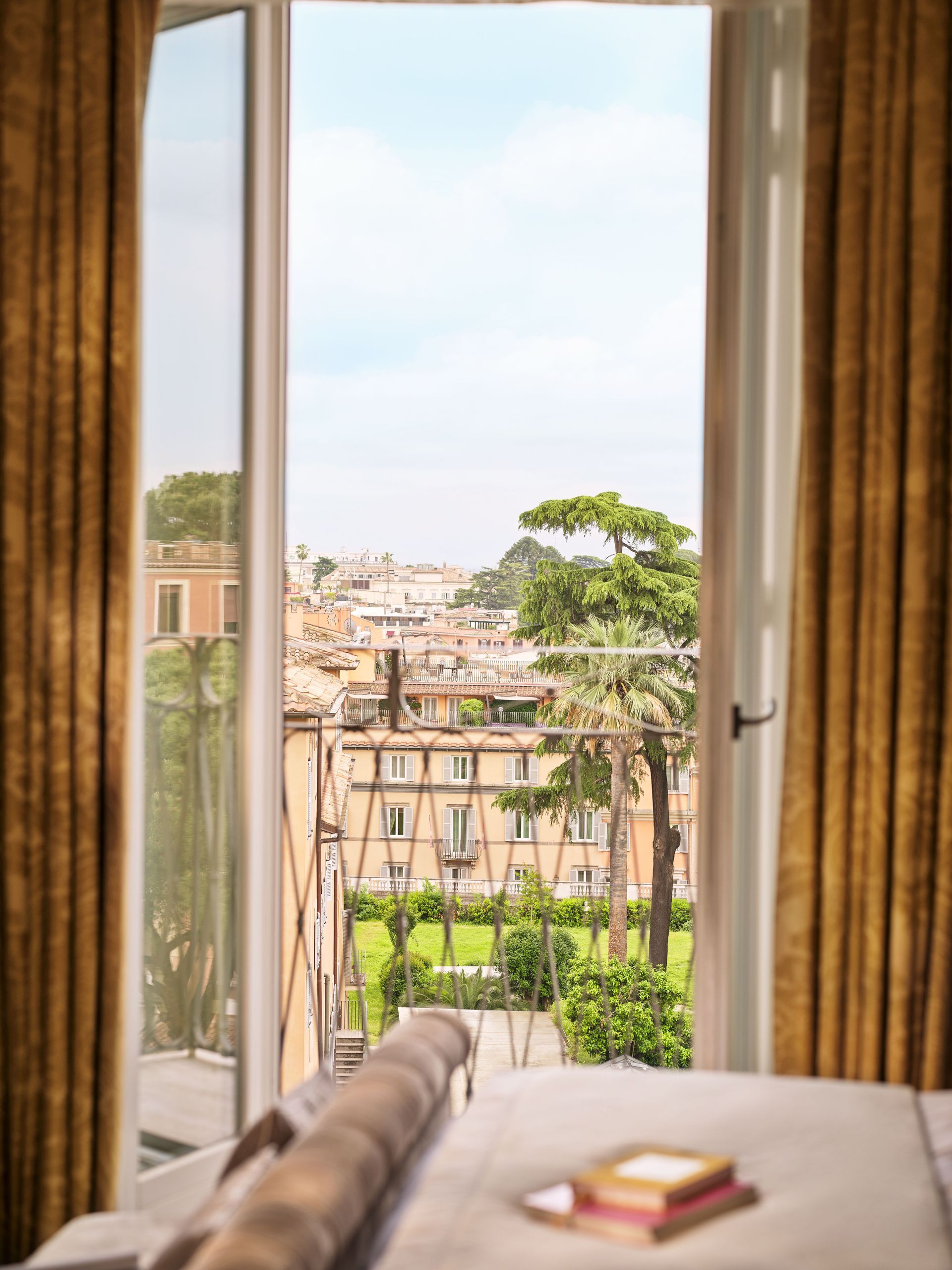 A bedroom with a view of Rome through an open window at the Dorchester Collection Hotel.