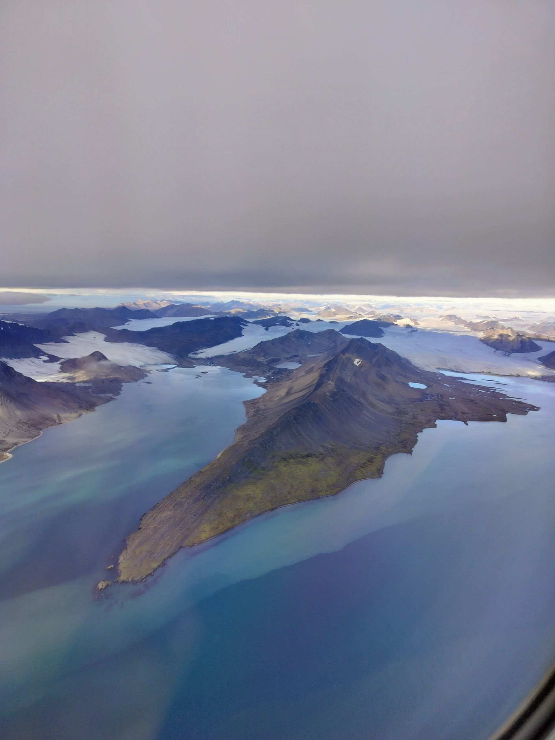 Aerial view of a mountainous island surrounded by blue water under a cloudy sky.