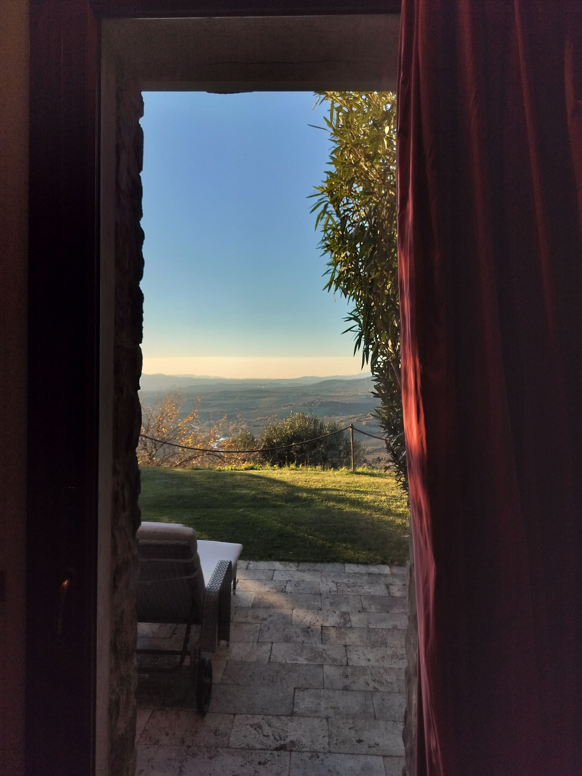 View through an open doorway of a landscape, blue sky, and red curtain.