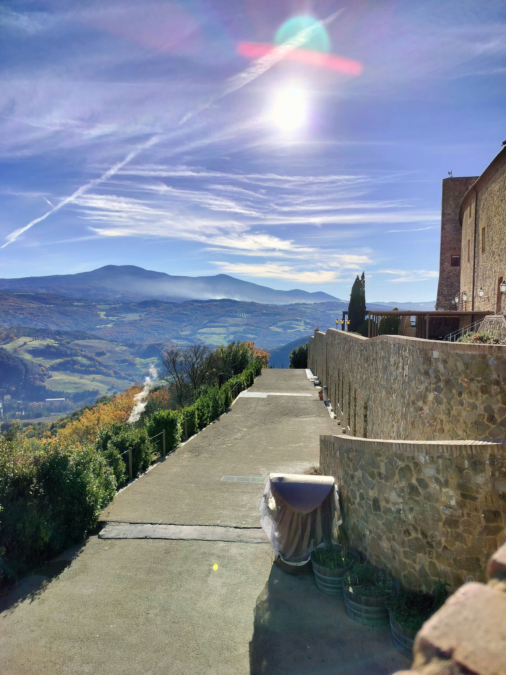 Stone pathway with a scenic view; sunlight, mountains, and vegetation.