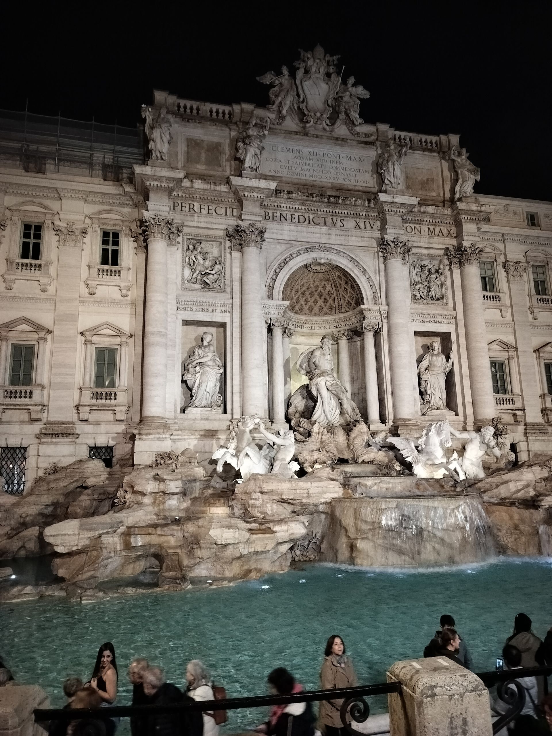 Trevi Fountain in Rome at night, illuminated, with figures and reflecting pool in the foreground.