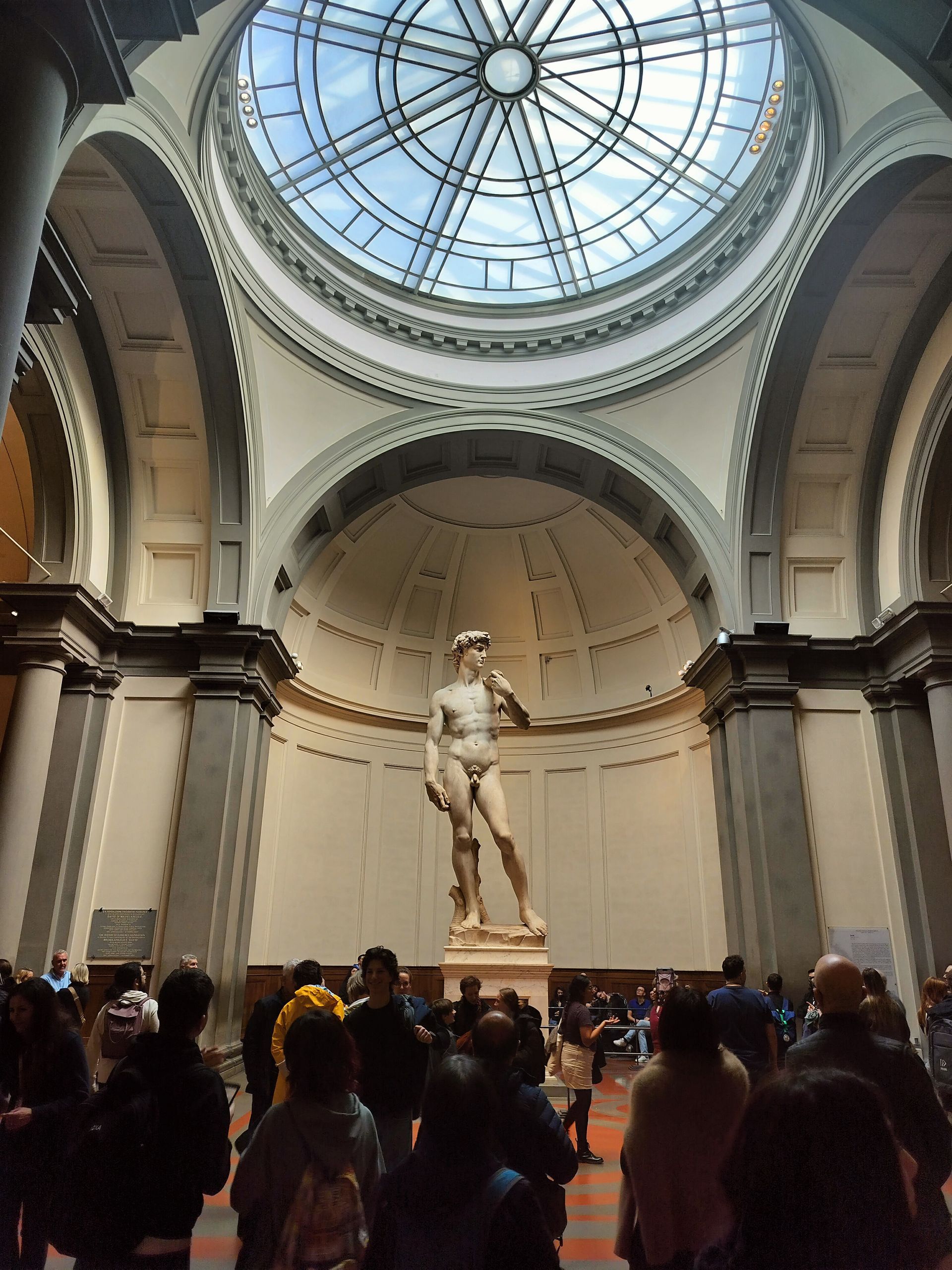 Michelangelo's David statue in a domed gallery, surrounded by a crowd of people.