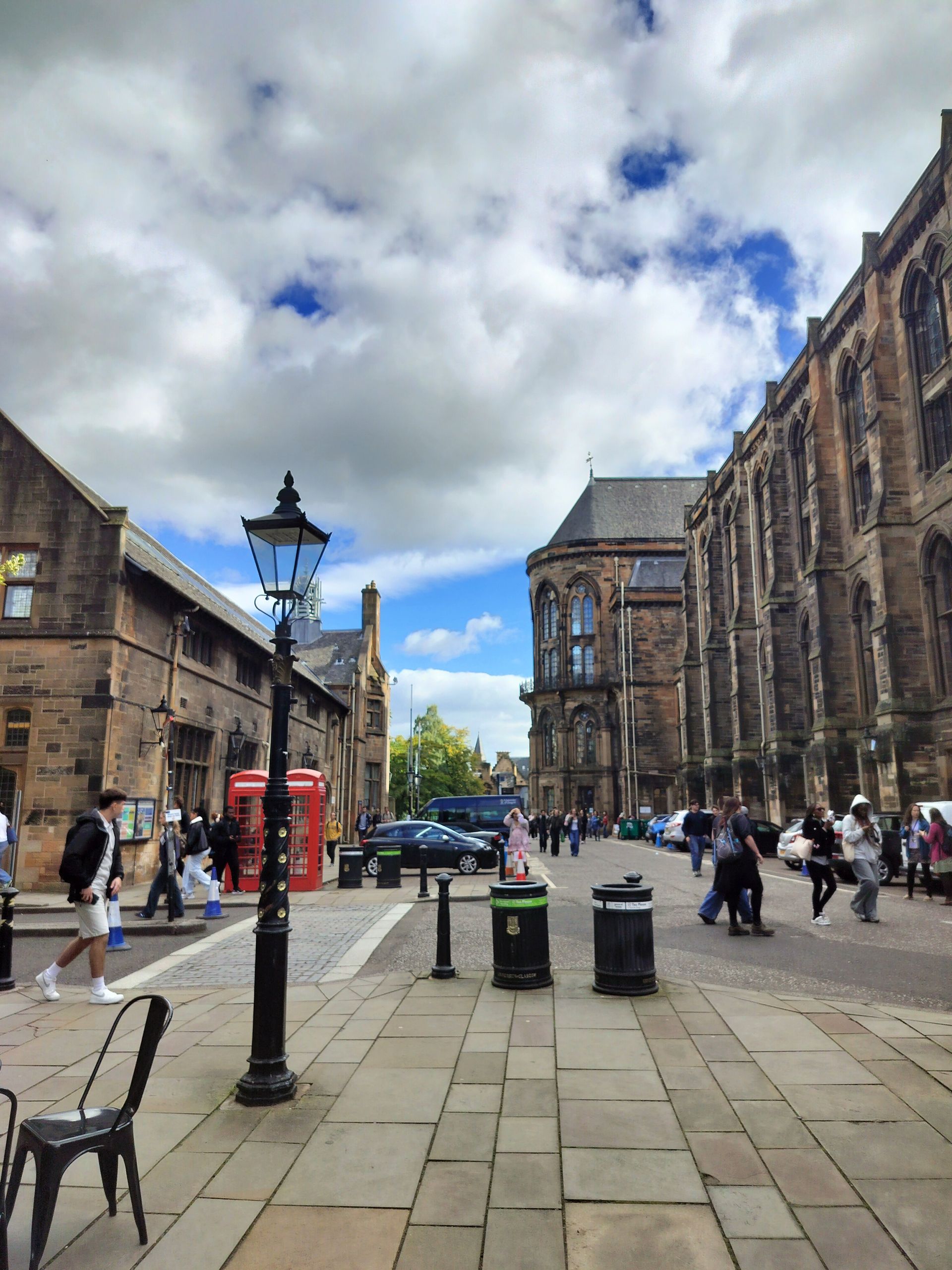 Cobblestone street with pedestrians, a red telephone box, and stone buildings under a cloudy sky.