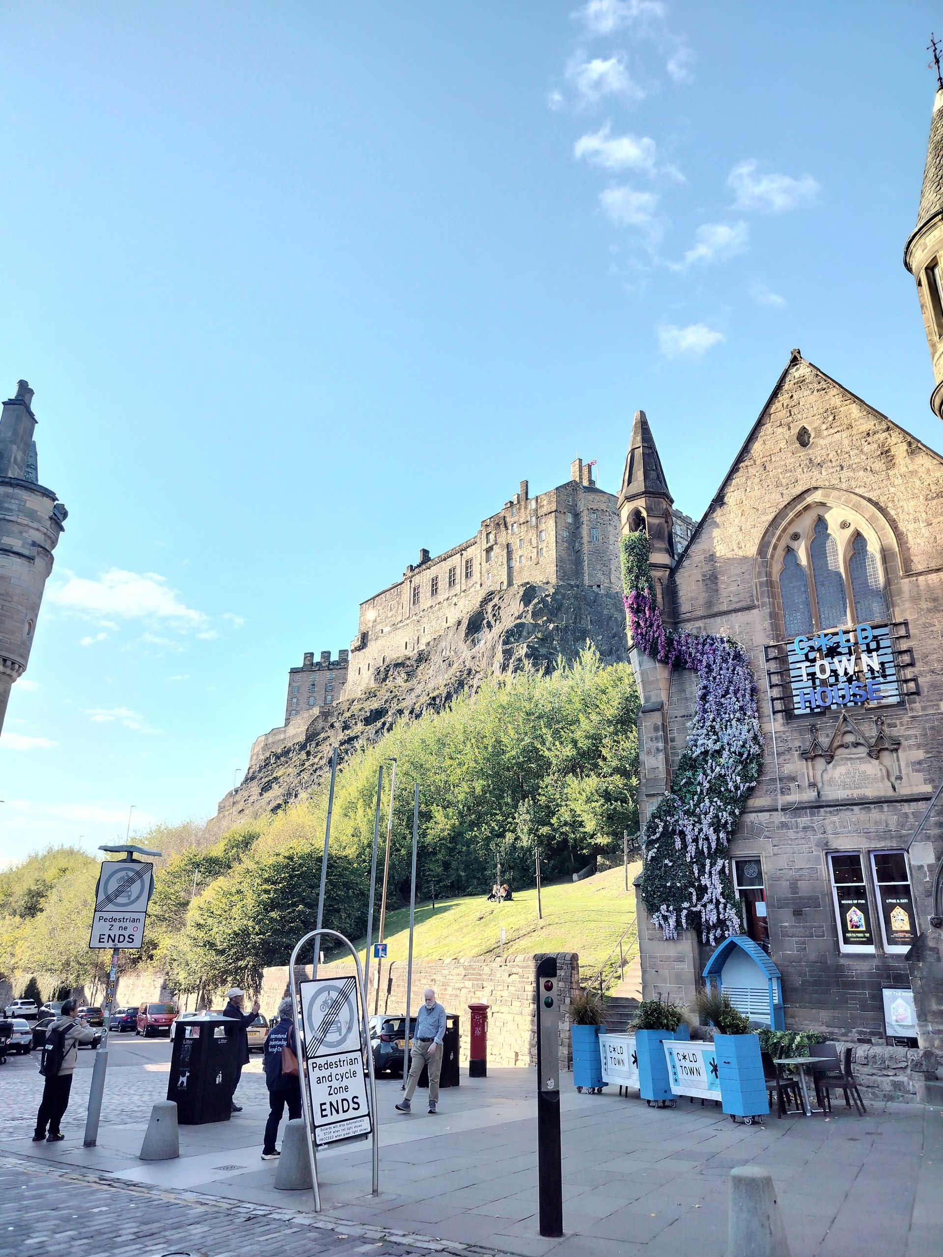 Edinburgh Castle atop a hill, viewed from a street with buildings, blue sky.