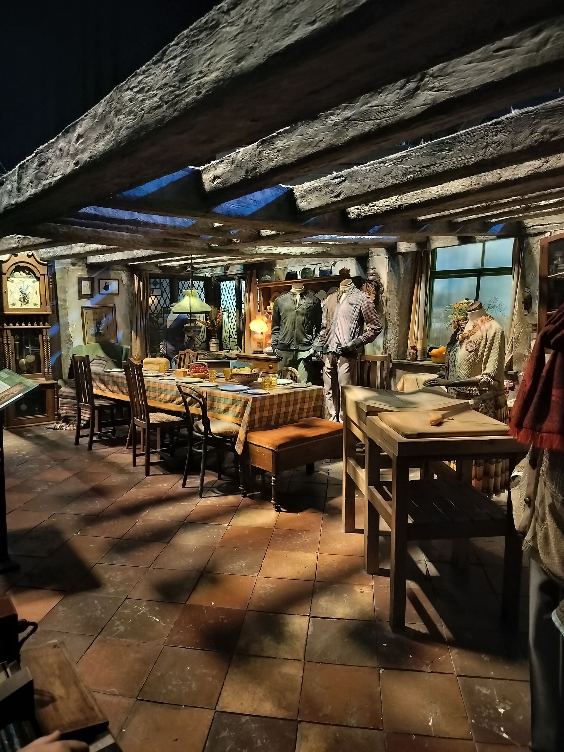 Interior of a rustic dining area with tables set, mannequins, and exposed wooden beams.