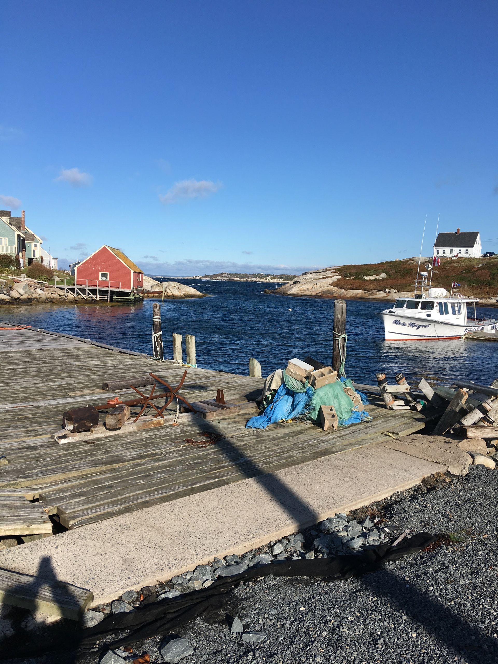 A weathered pier overlooks a harbor with a red building, small boat, and blue water under a clear sky.