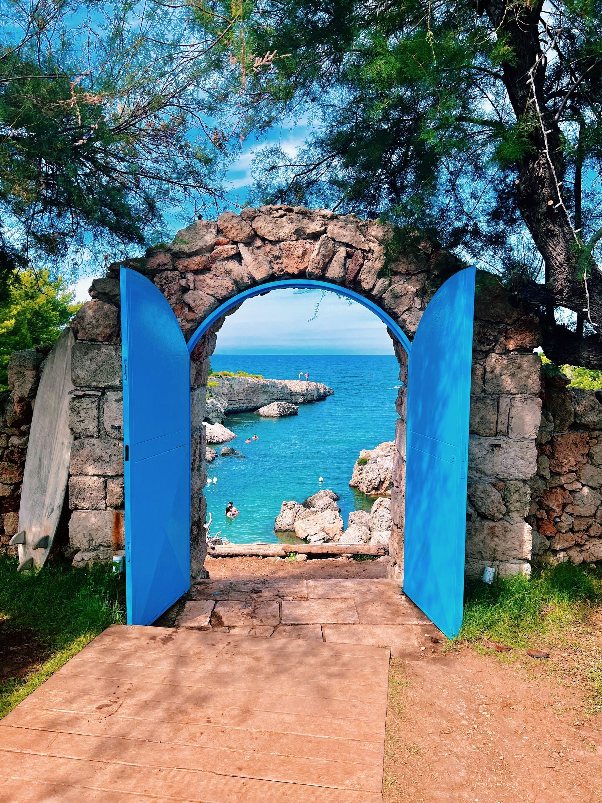 A stone archway with blue doors leading to the ocean in Puglia, Italy.