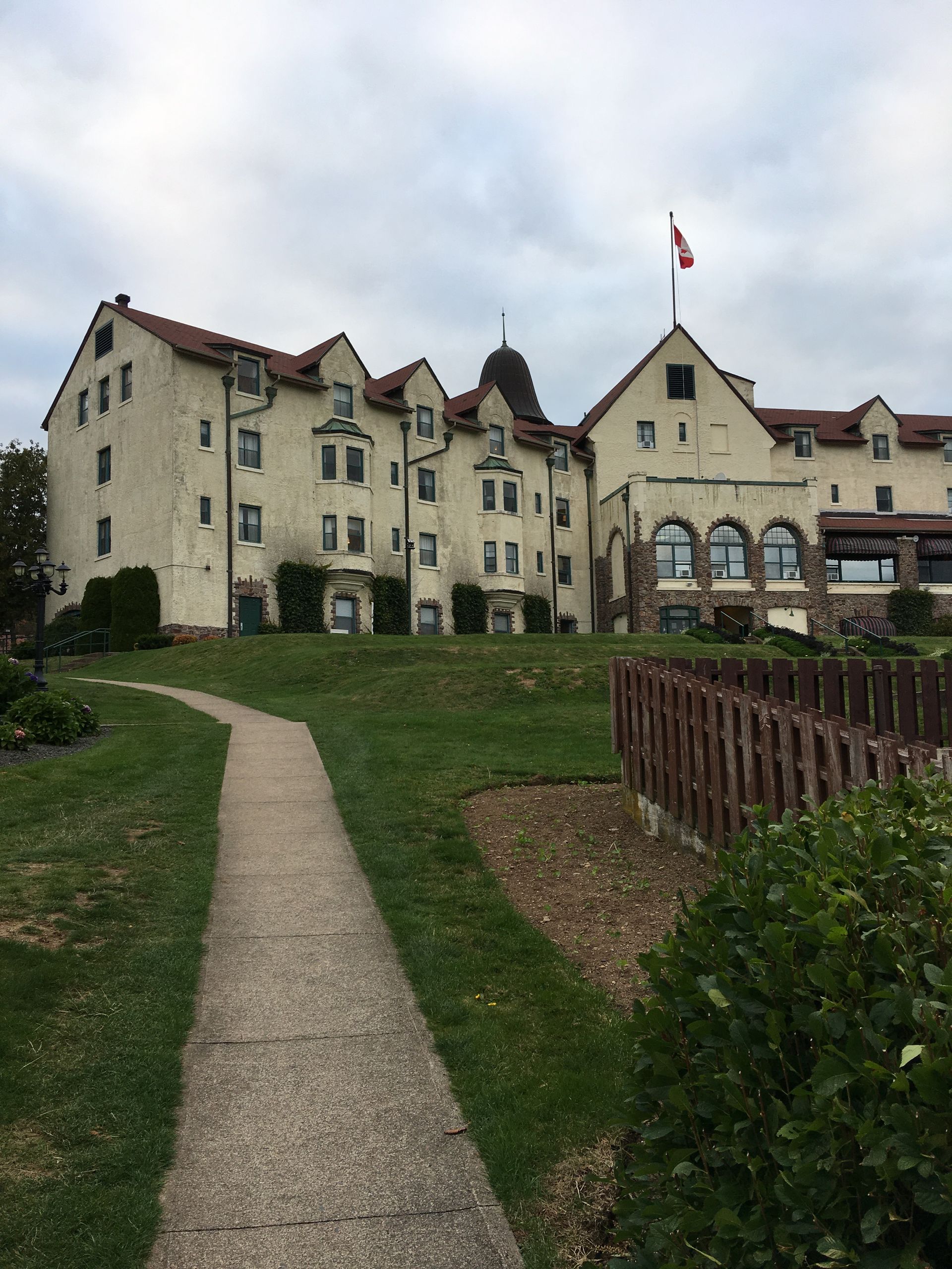 Stone building with a flag on the roof; pathway leading up a grassy hill.