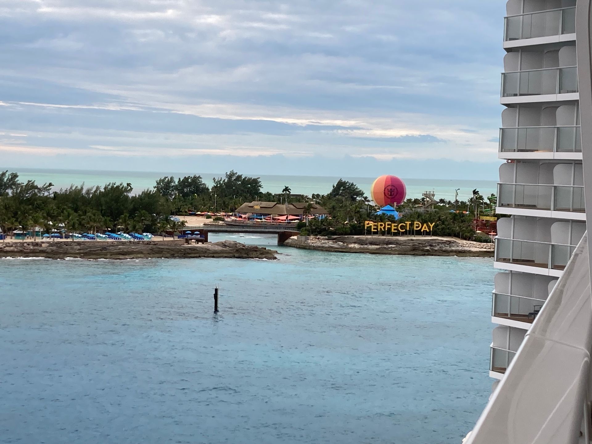 A water view with a shoreline, bridge, and a colorful hot air balloon. A white balcony is on the right.