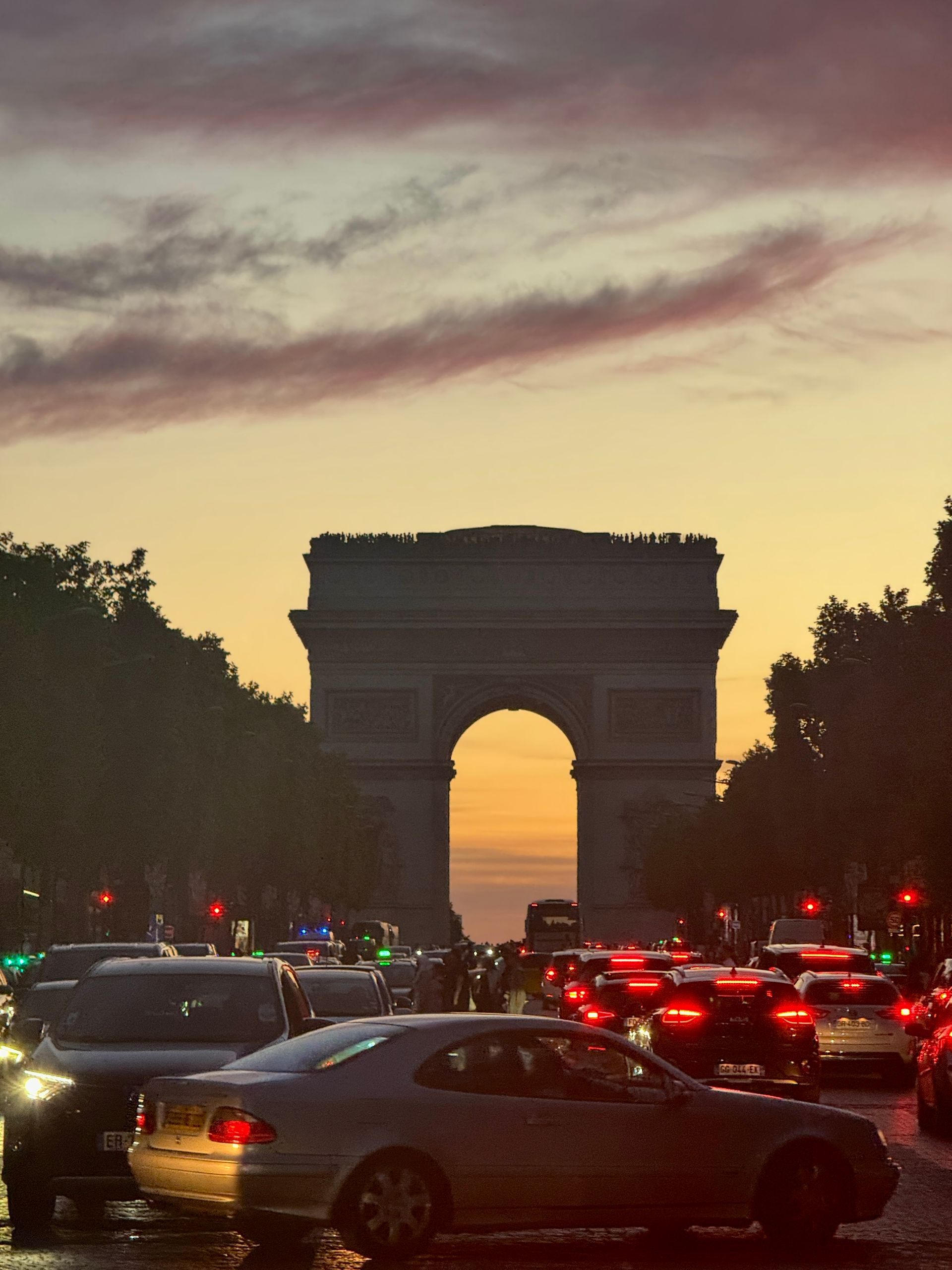 A busy street with the Arc de Triomphe in the background at sunset in Paris, France.