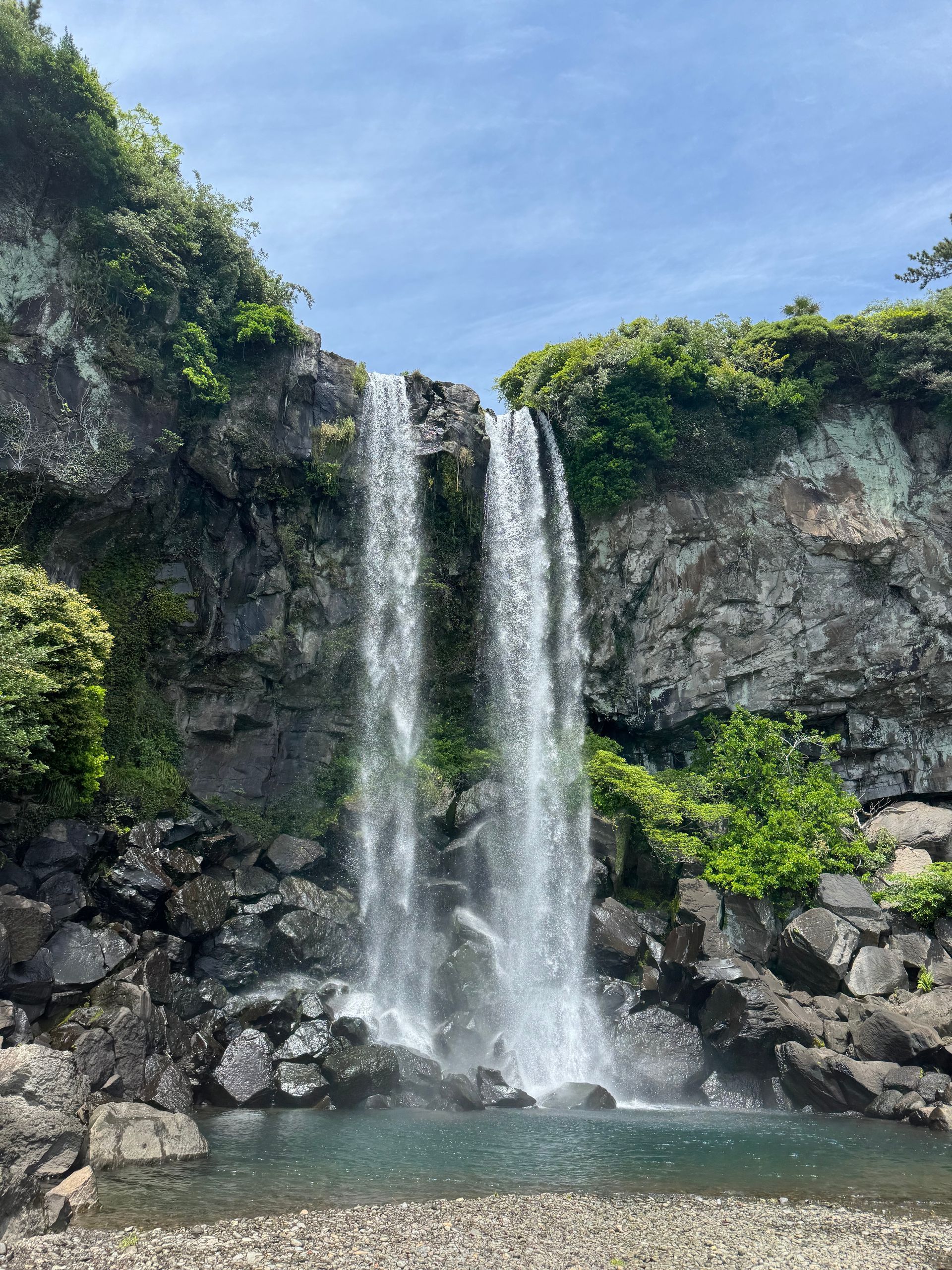 Waterfall cascading down a rocky cliff into a pool of water on Jeju Island, South Korea.