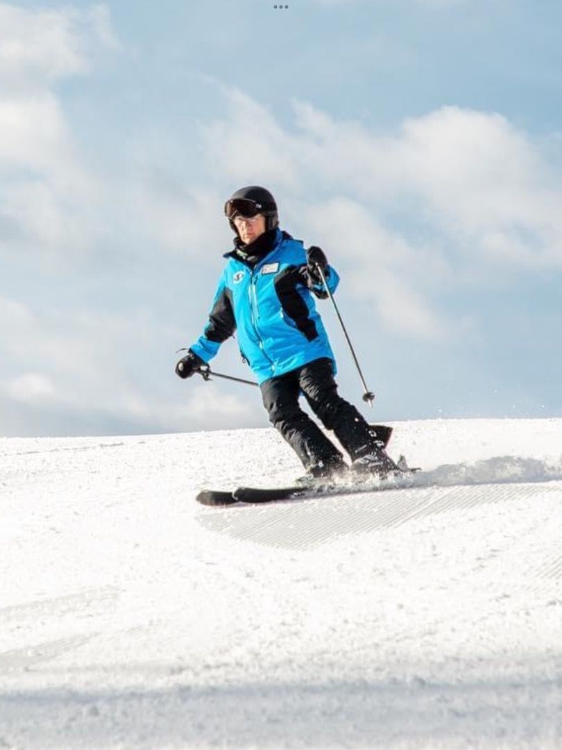 Skier in blue jacket, skis down a snow-covered slope on a sunny day.