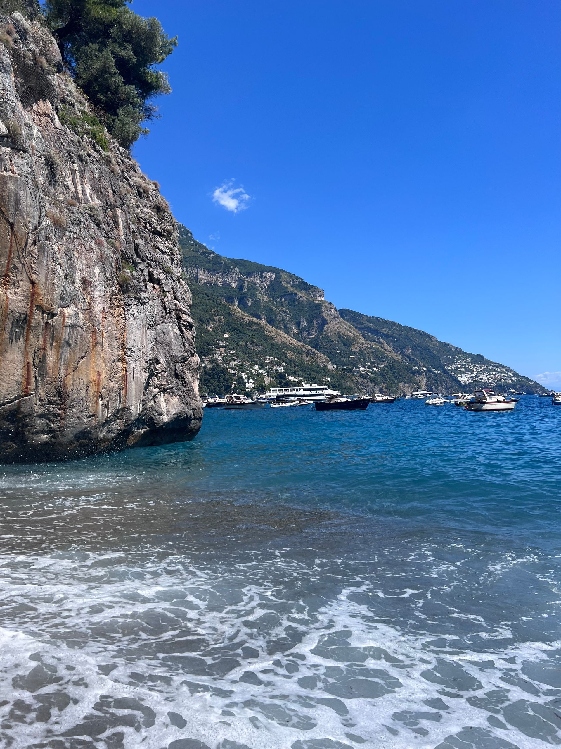 A boat is floating on the water near a rocky cliff in the Amalfi Coast, Italy.