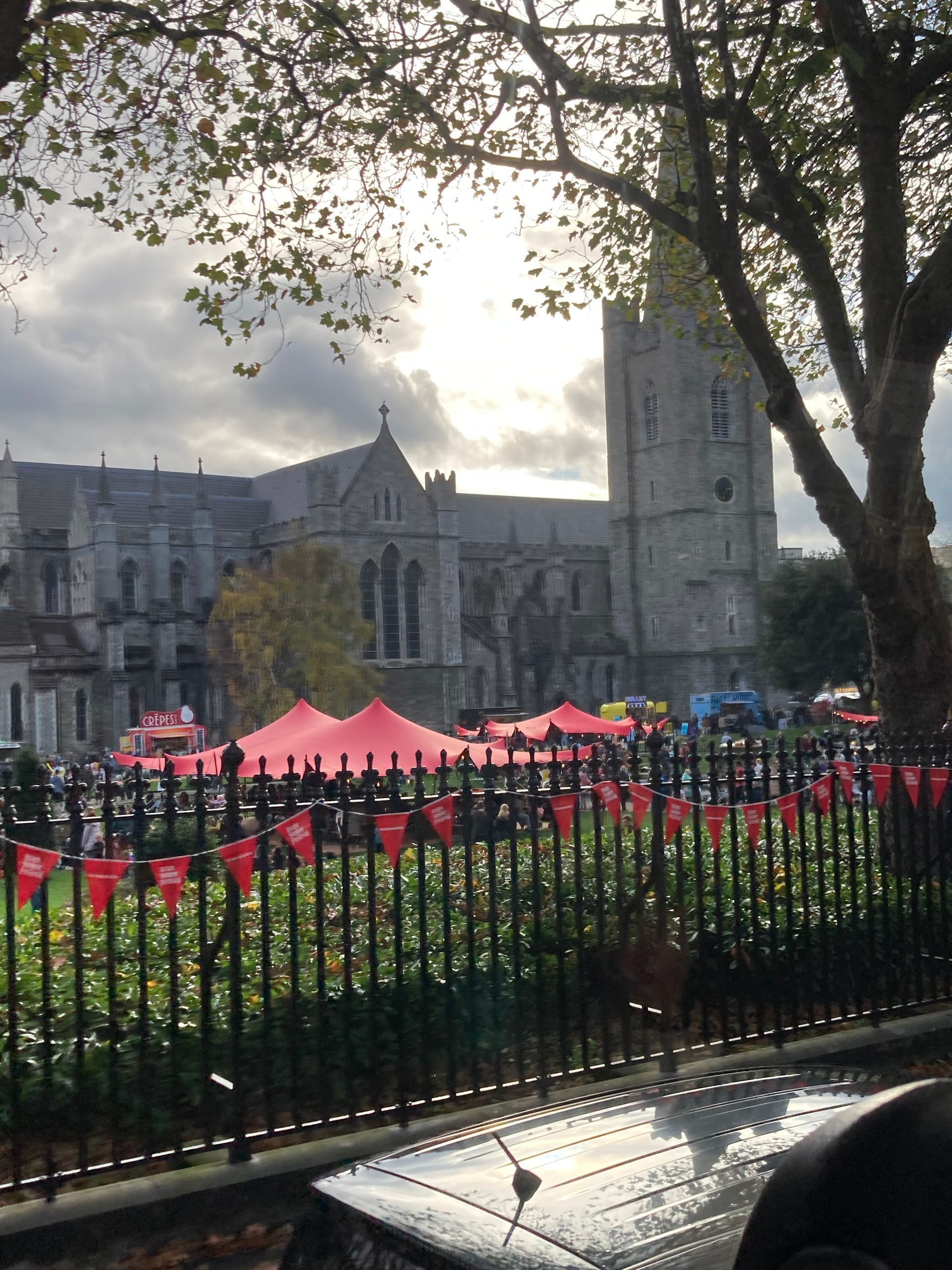 A cathedral with a tall tower behind red tents and a black fence, under a cloudy sky.