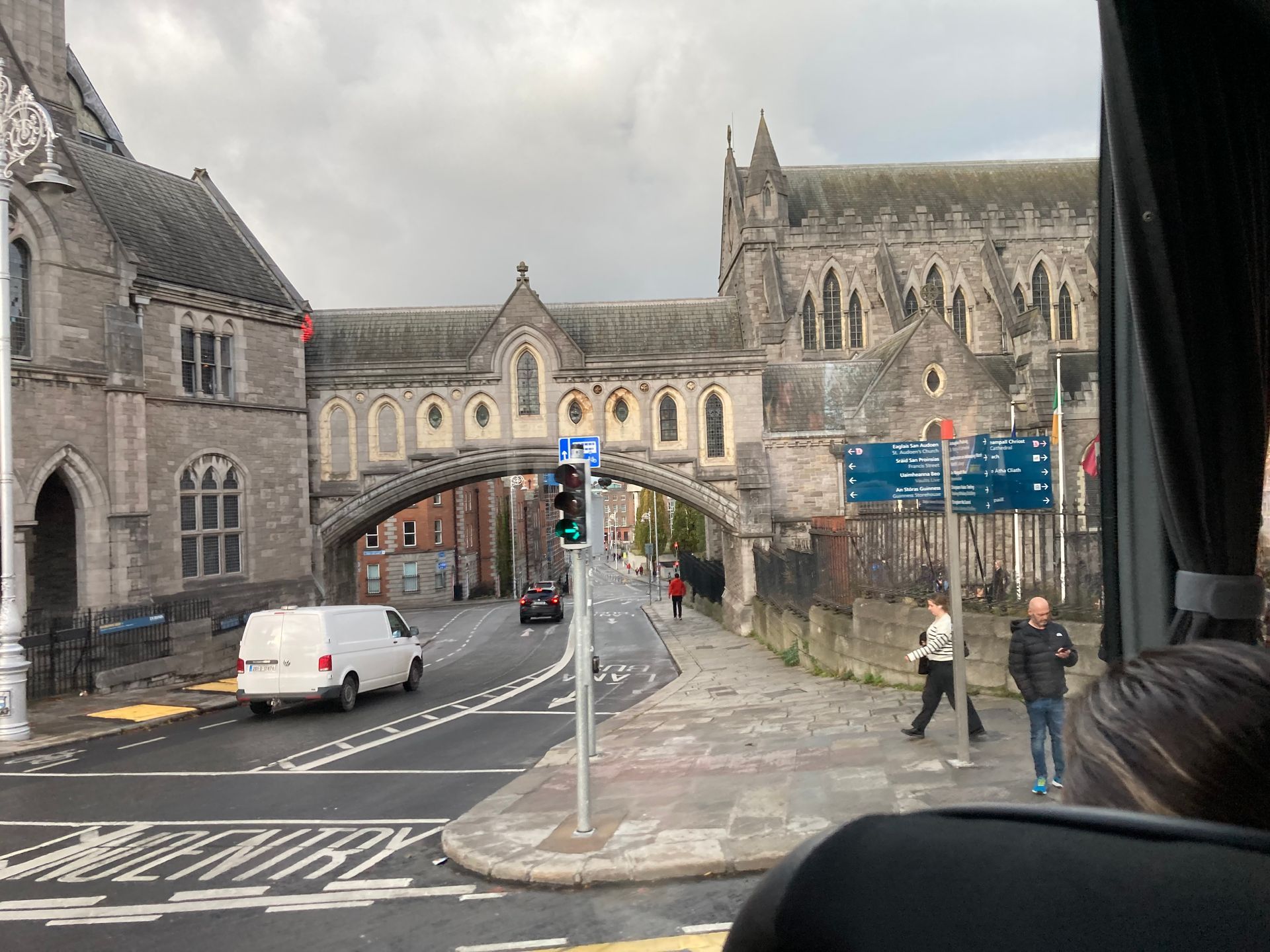 Street scene with a cathedral, pedestrian bridge, and vehicles in Dublin, Ireland. Cloudy sky.
