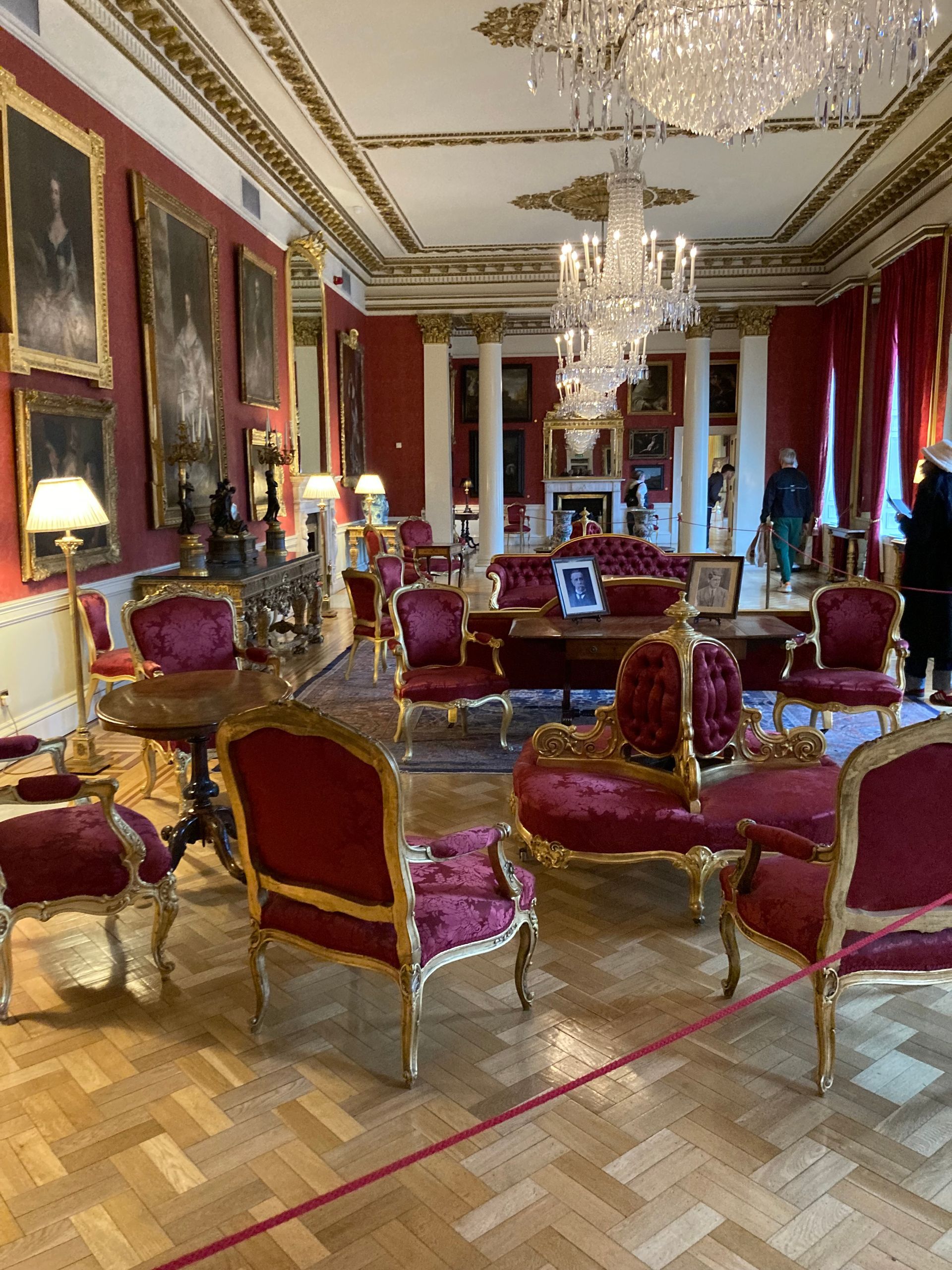 Luxurious red and gold room with ornate furniture, chandeliers, and portraits, possibly a palace interior.