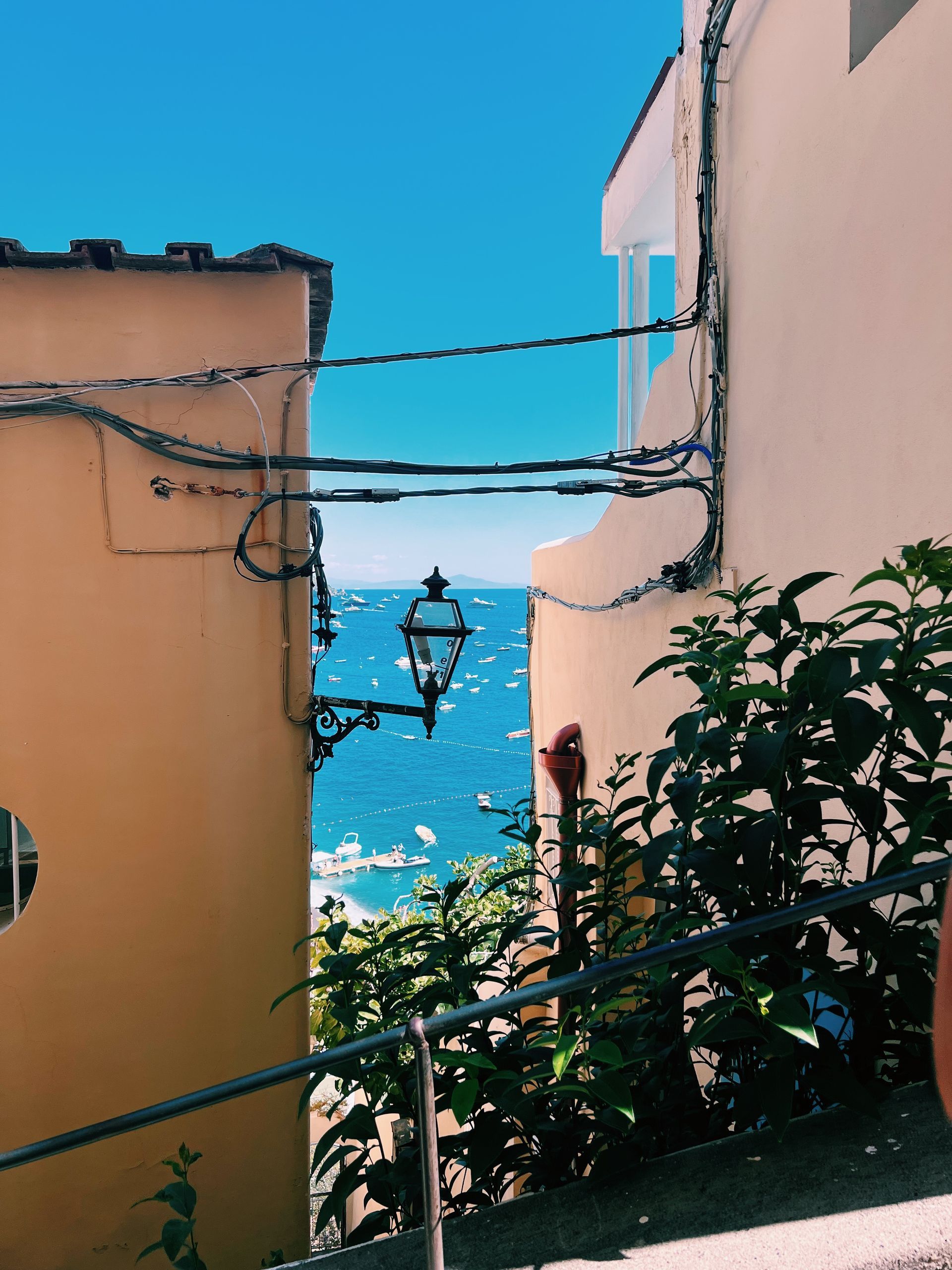 A street light hangs between two buildings overlooking the ocean in the Amalfi Coast, Italy.