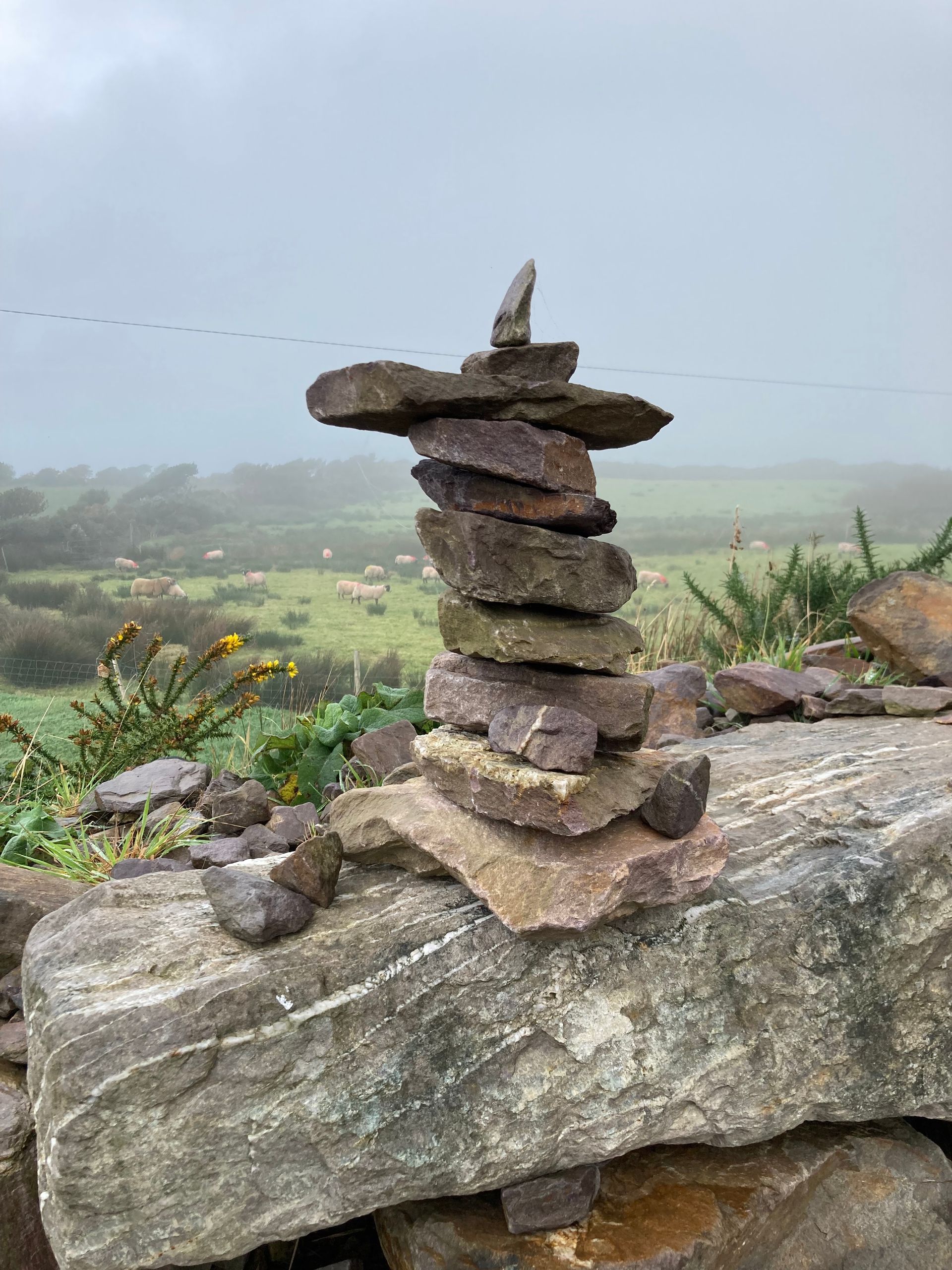 Stone cairn on a rock wall, misty green field in the background.
