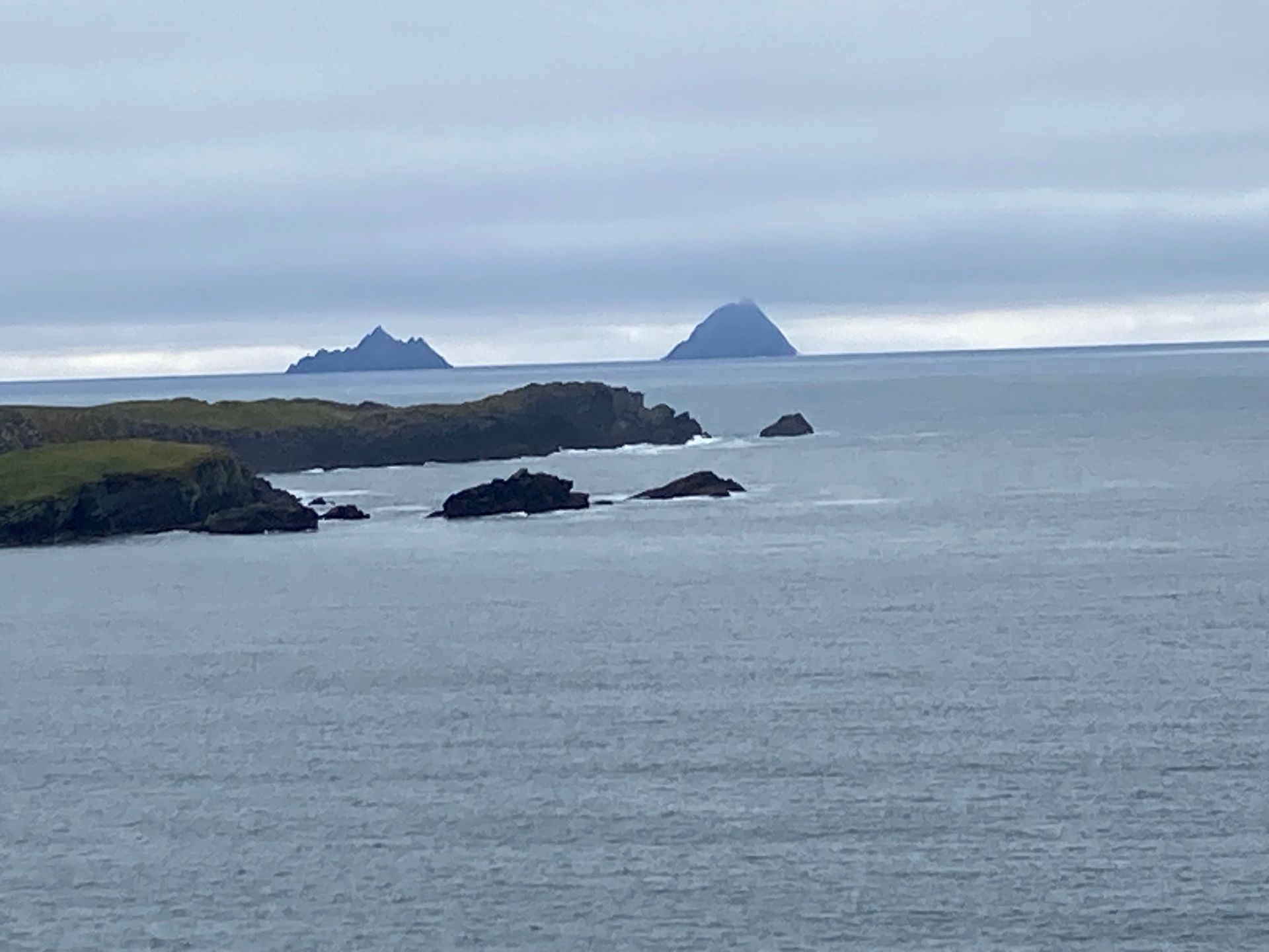 Rocky coastline with two distant, cone-shaped islands under a cloudy sky.