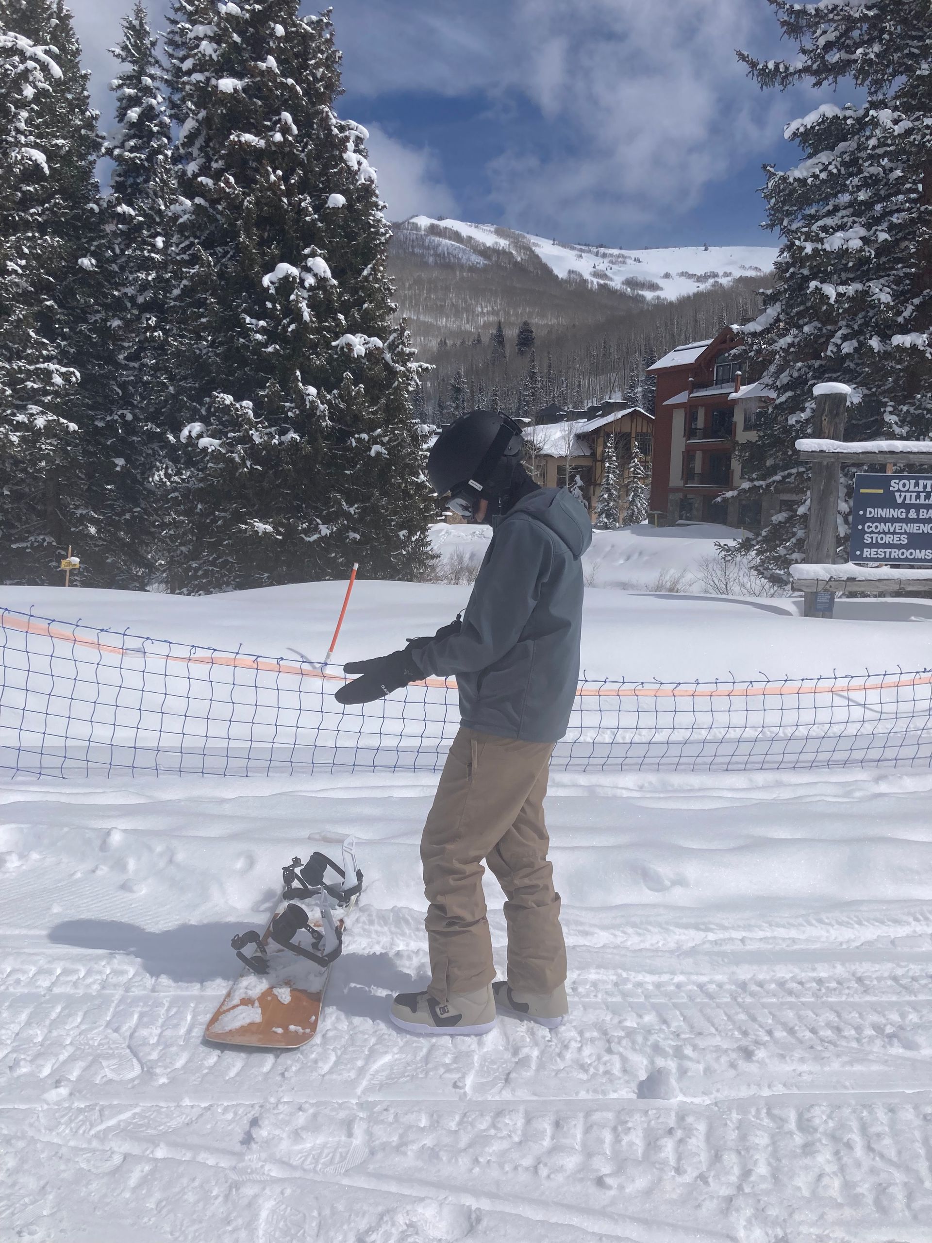 Person with a snowboard in a snowy area, mountain background. Pointing to something.