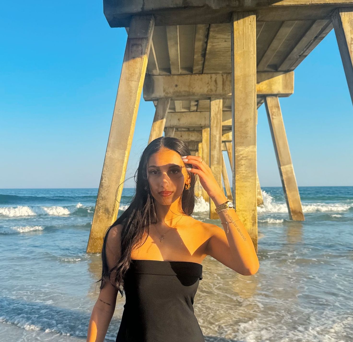 A woman in a black dress is standing under a pier