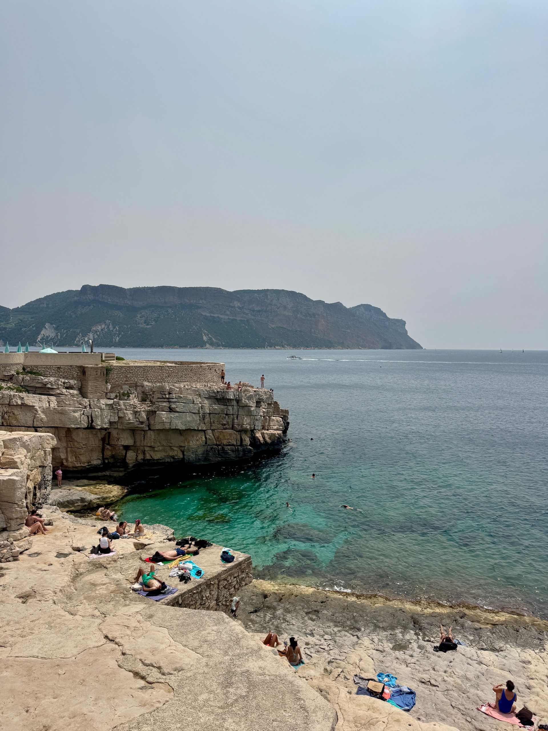 A group of people are sitting on the beach near the ocean in Cassis, France.