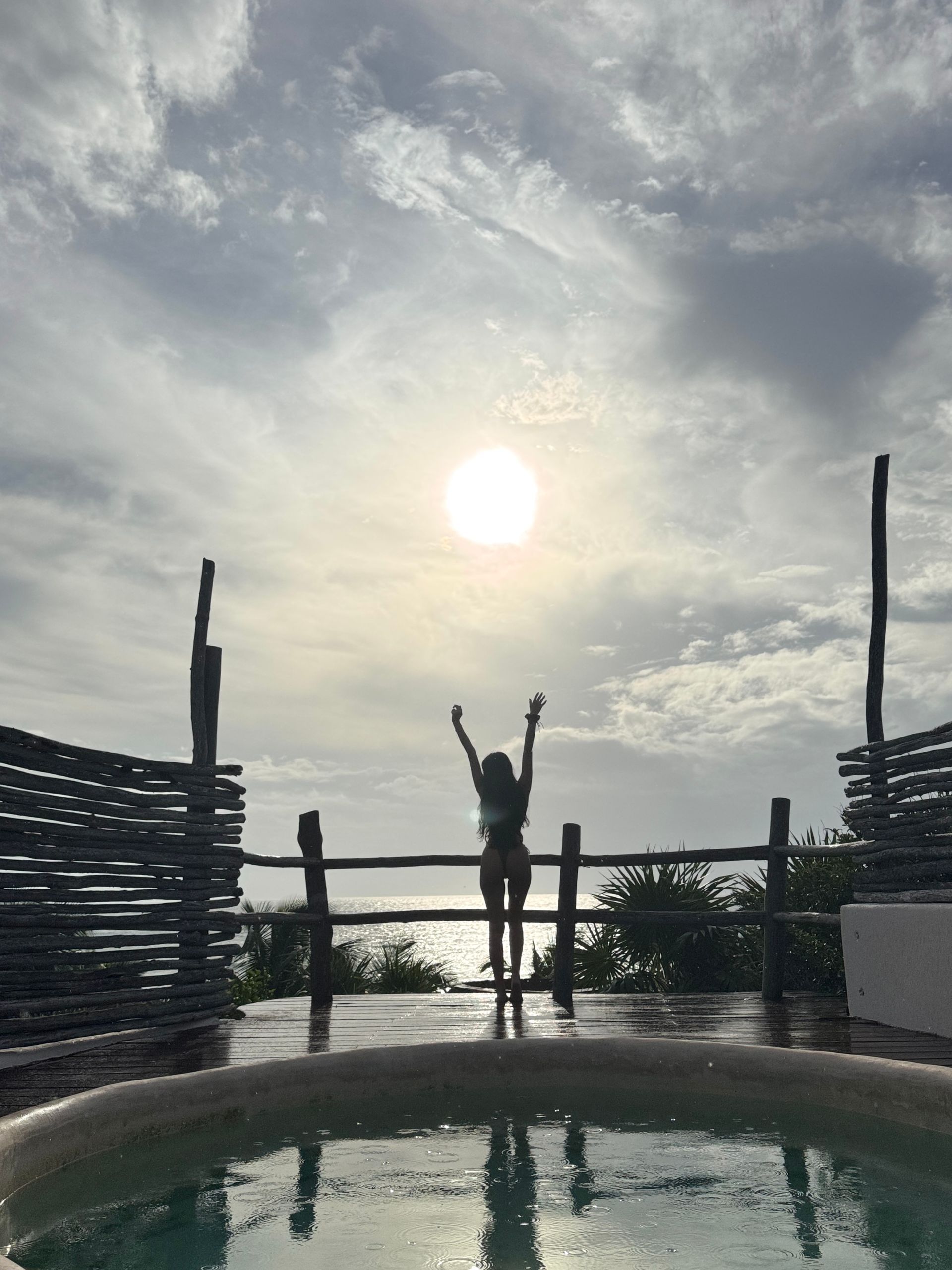 A woman in a bikini is standing in a pool with her arms in the air at Papaya Playa Project hotel in Tulum, Mexico.