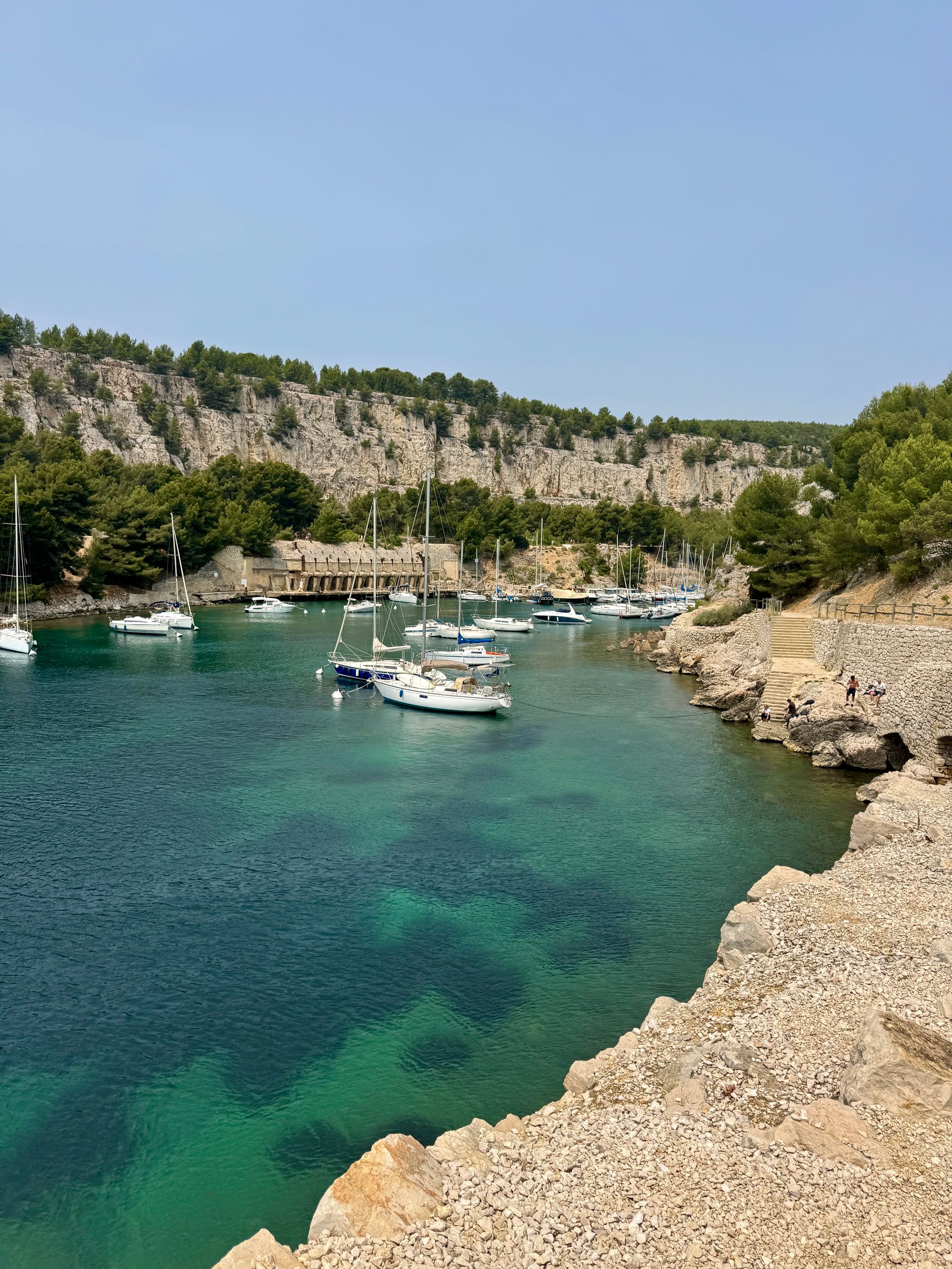 A body of water with boats in it and a cliff in the background at the Calanques in Cassis, France.