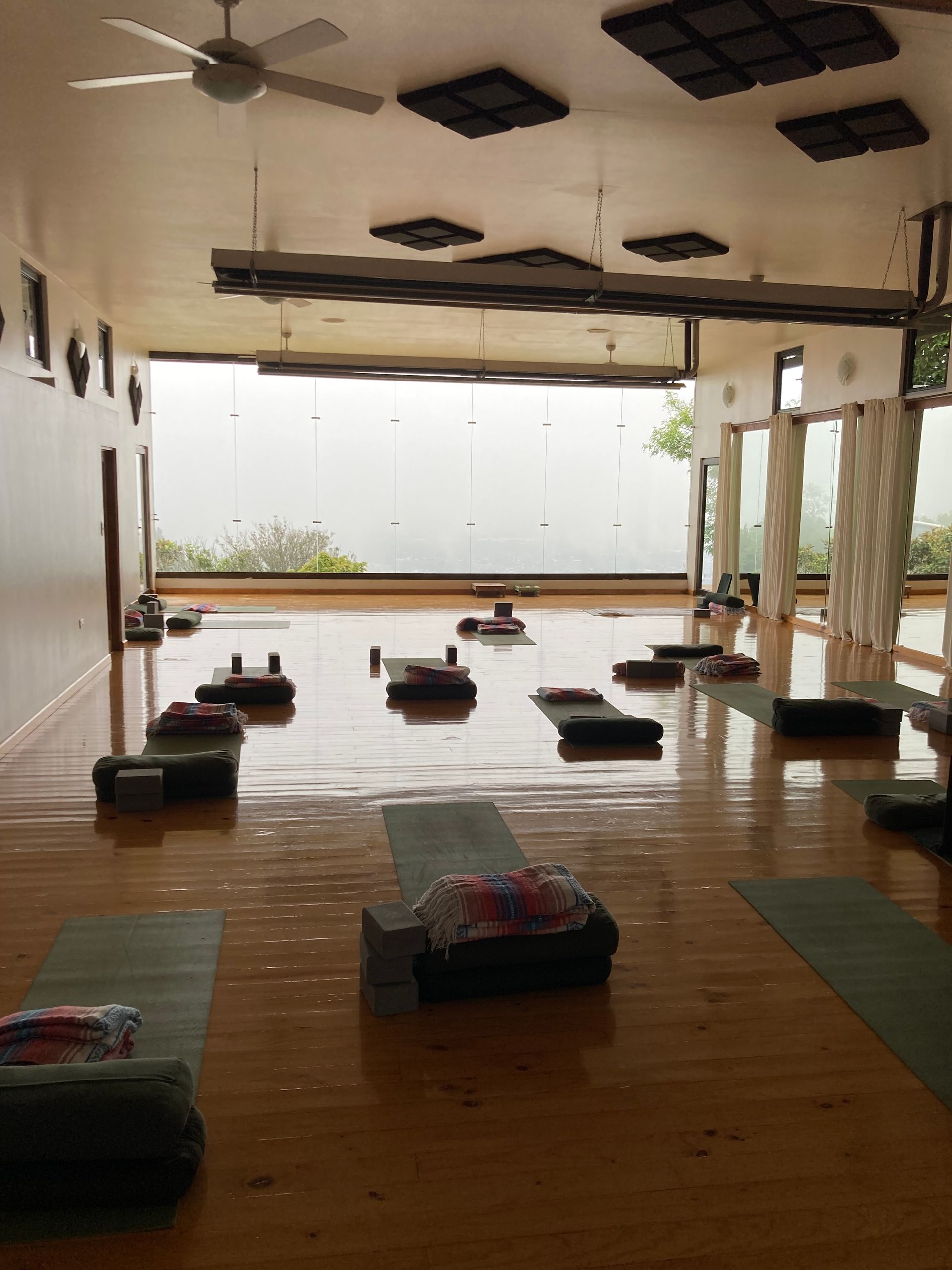 Yoga studio with mats, blocks, and pillows on a wood floor, large windows.