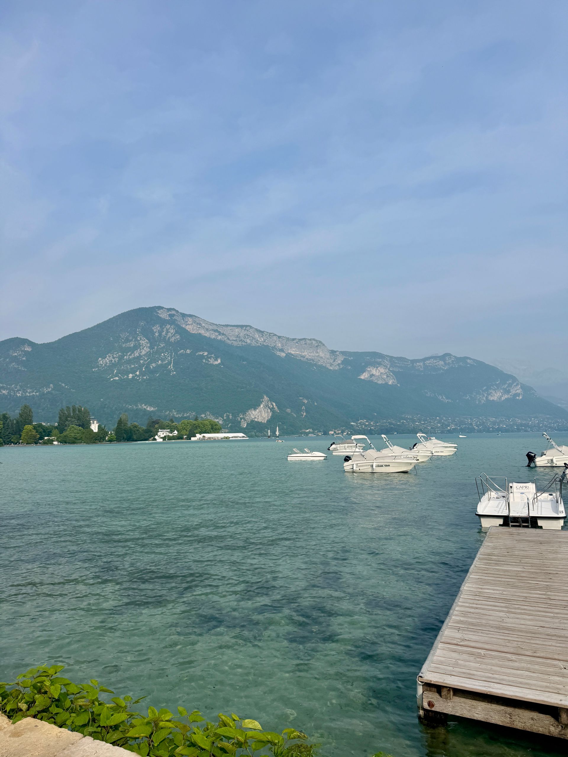 A dock with boats docked in Lake Annecy with mountains in the background in France.